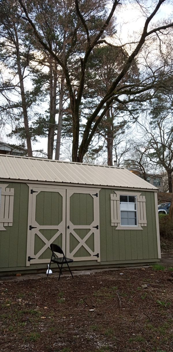 Small green shed with white trim and a window in a community yard.