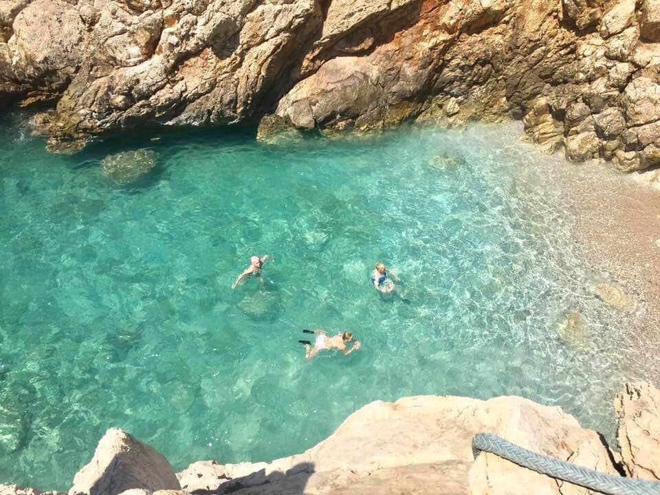 People swimming in clear turquoise water near rocky coast.