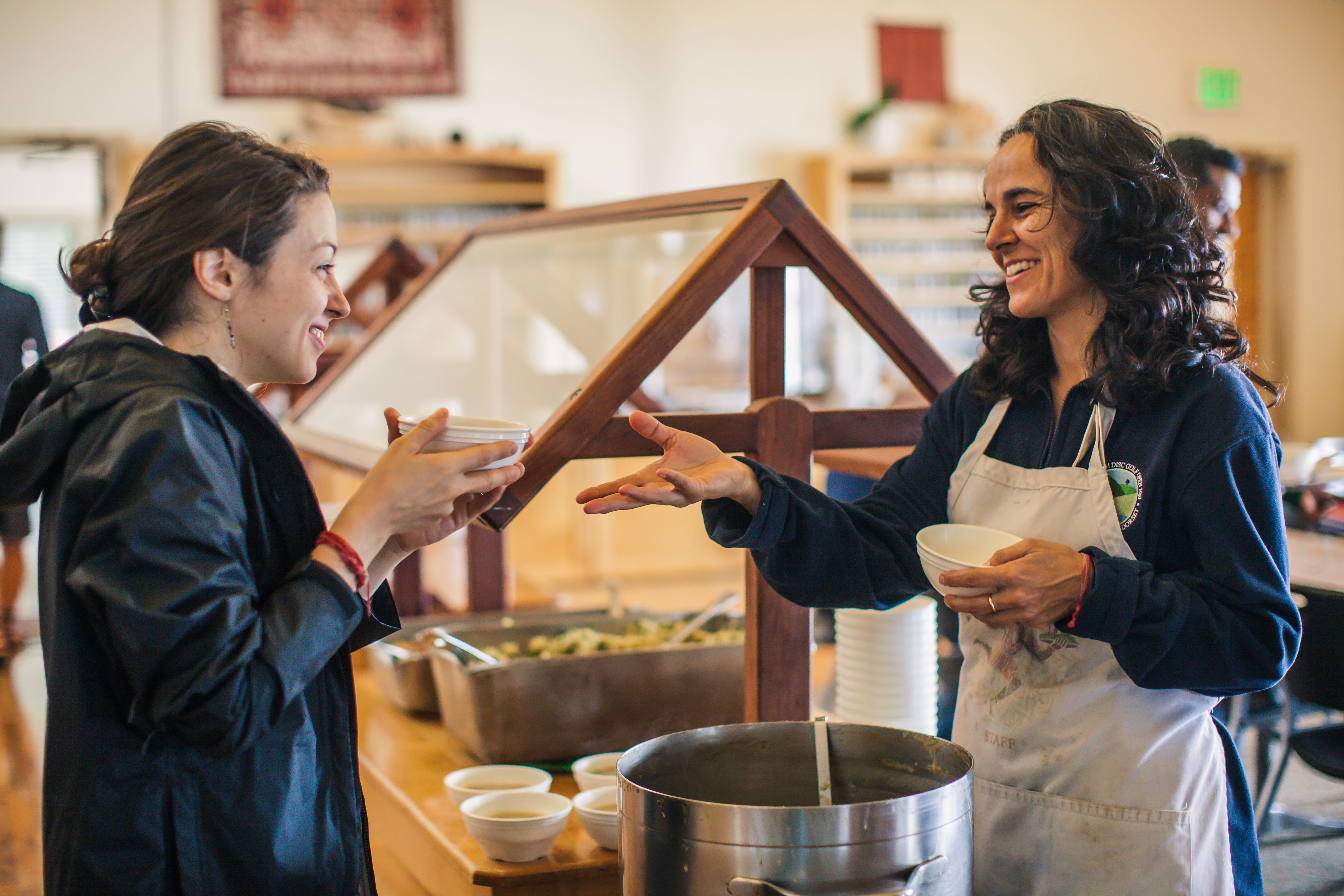 Two women exchanging food at a community kitchen event.