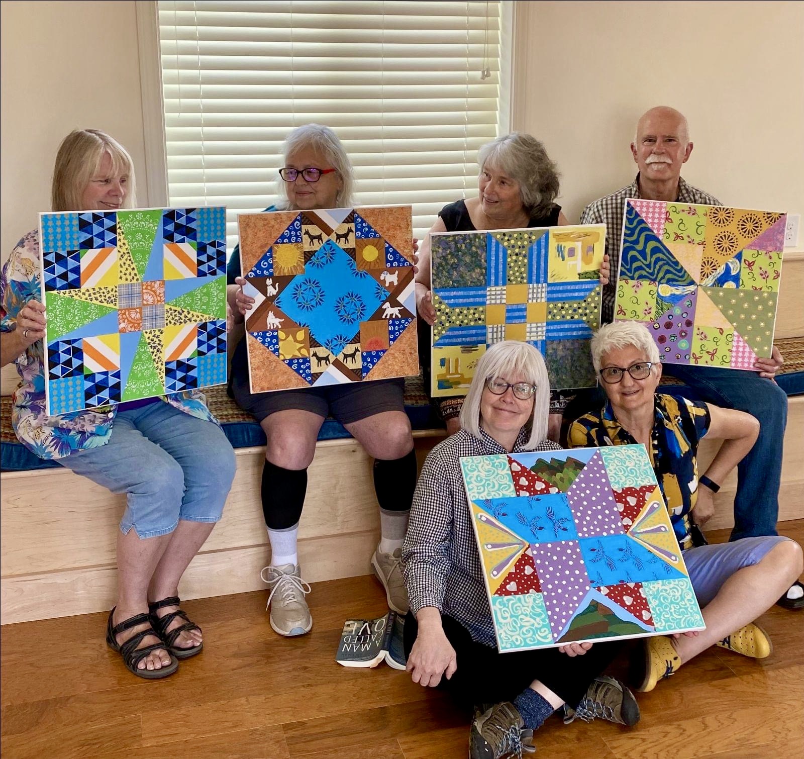 Women holding colorful quilt art pieces in a cozy room.