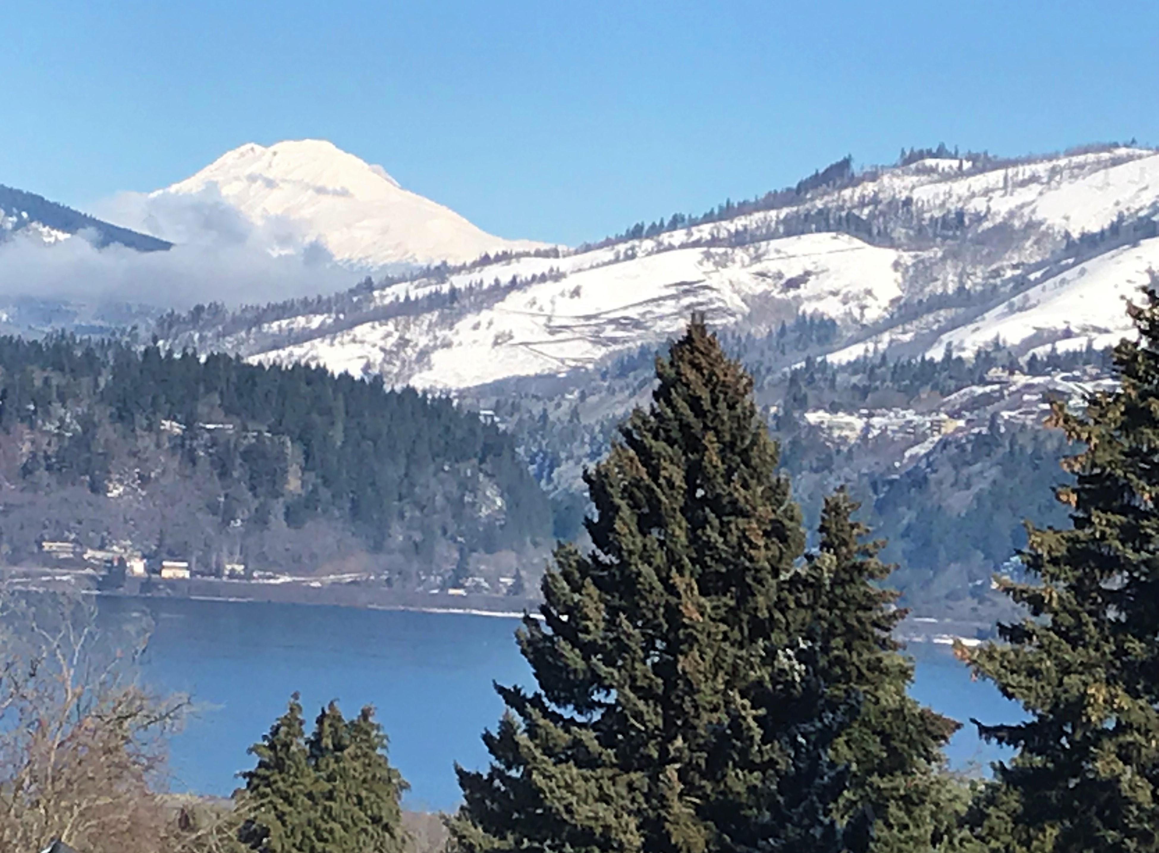 Beautiful landscape with snow-covered mountains, lake, and evergreen trees.