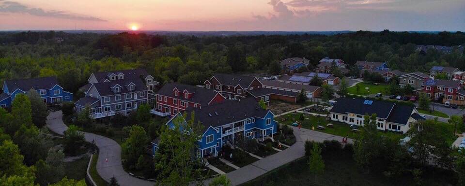 Aerial view of cohousing community at sunset with colorful homes and green spaces.