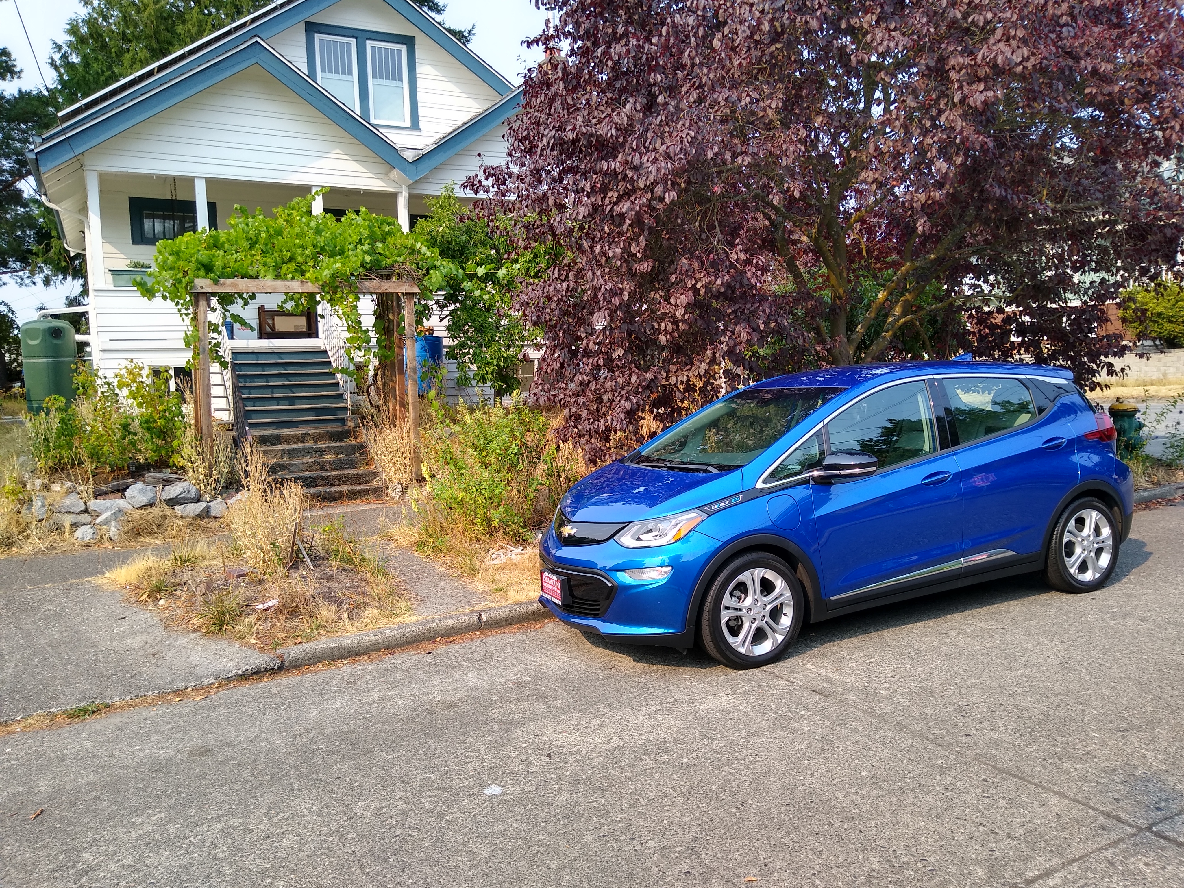 Blue electric car parked near a cozy community house with lush trees.