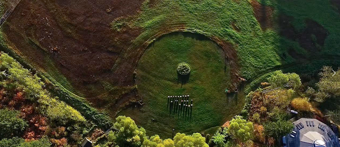 Aerial view of a lush green park with a circular monument and surrounding trees.