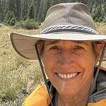 Person smiling outdoors with hat in natural setting for community building.