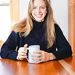 Smiling woman with long hair holding a coffee mug indoors.