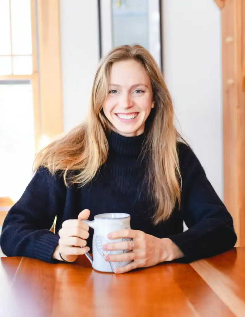Smiling woman with long hair holding a coffee mug indoors.