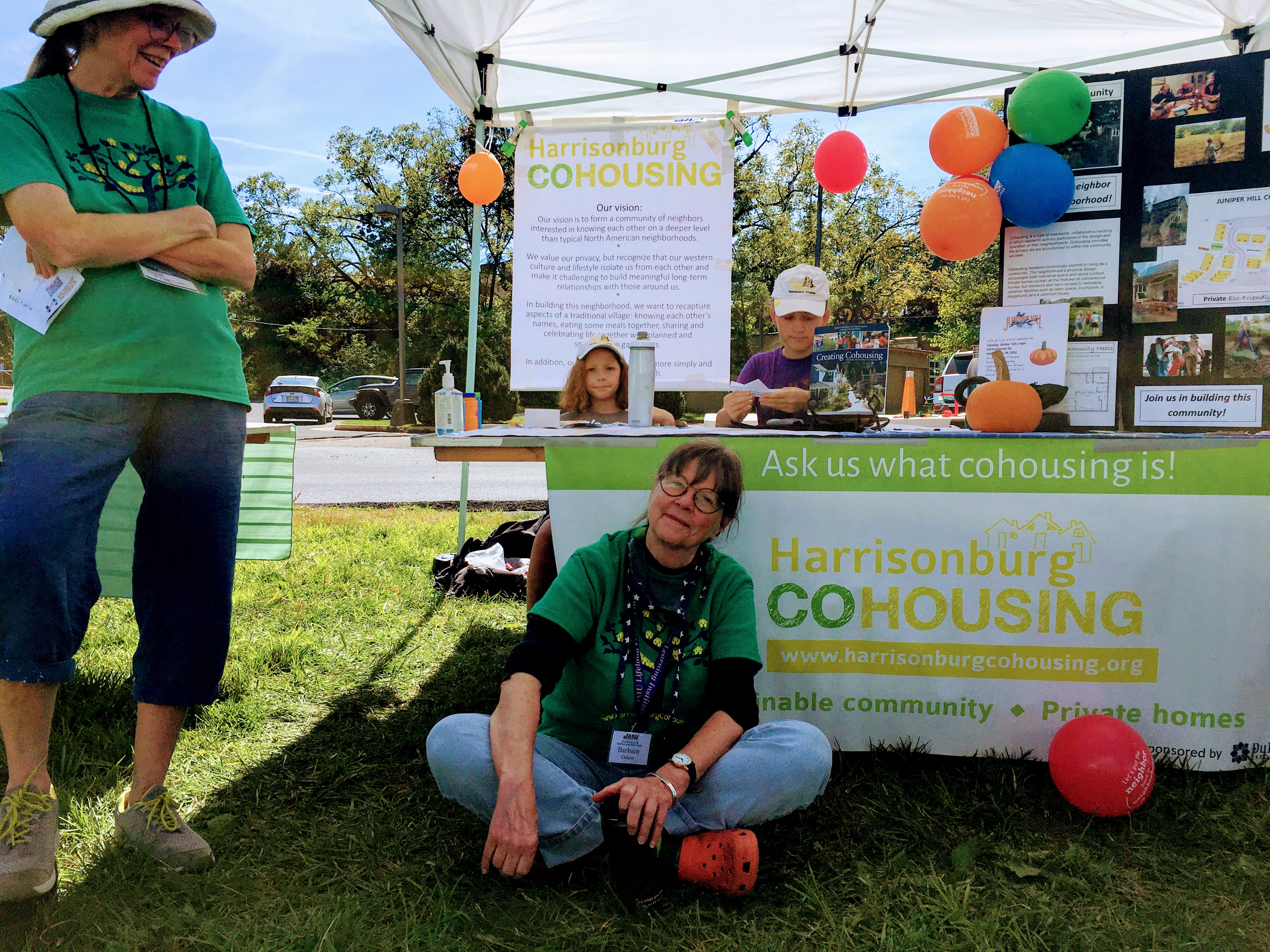 Harrisonburg Cohousing booth at community event with colorful balloons and informational posters.