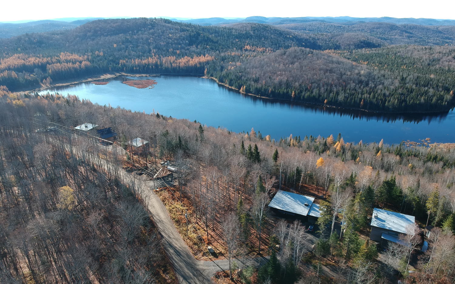 Aerial view of a forested landscape with a lake and cabins.
