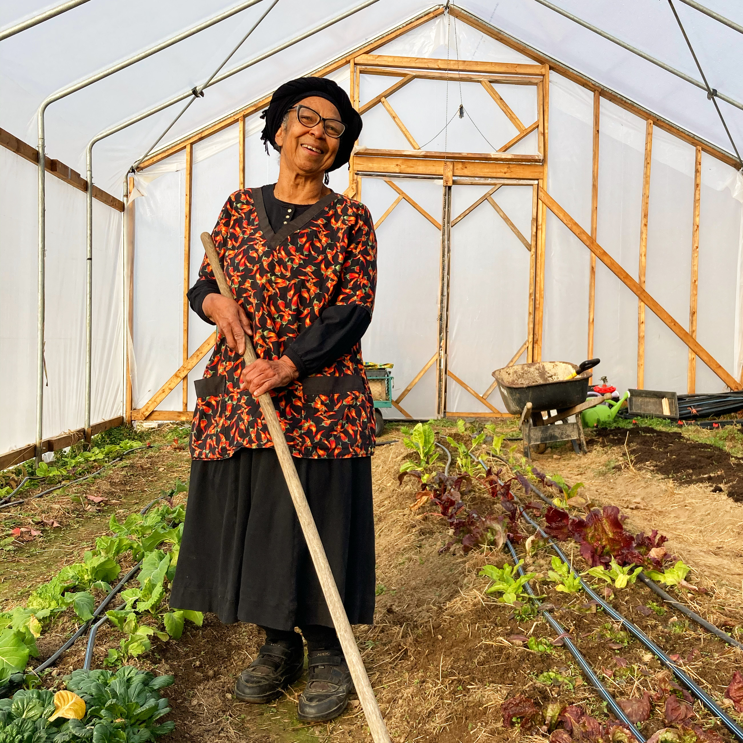 Woman smiling in greenhouse with garden beds and tools.