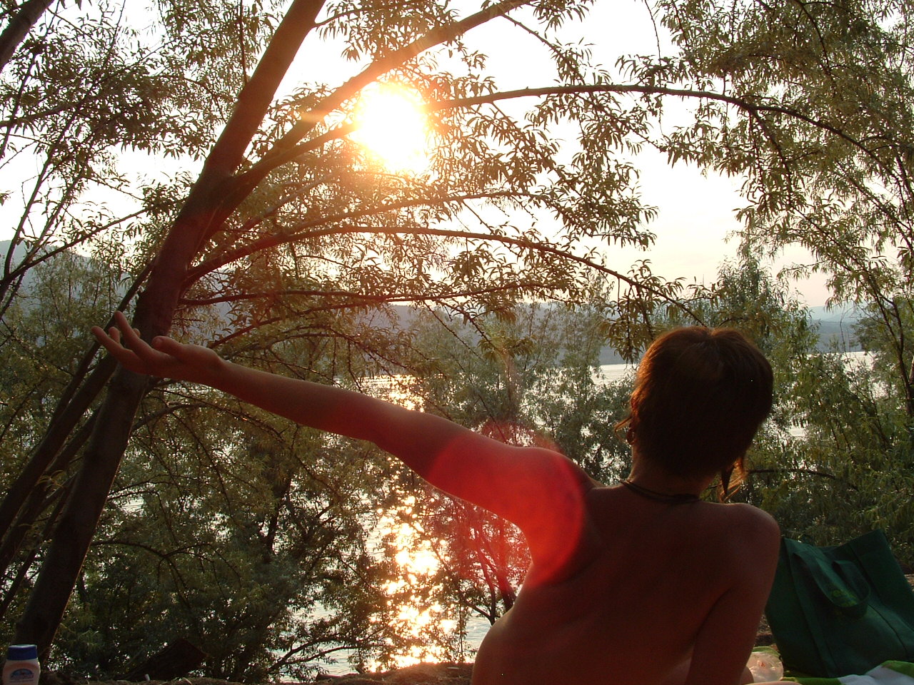 Person practicing yoga outdoors near a lake at sunset.