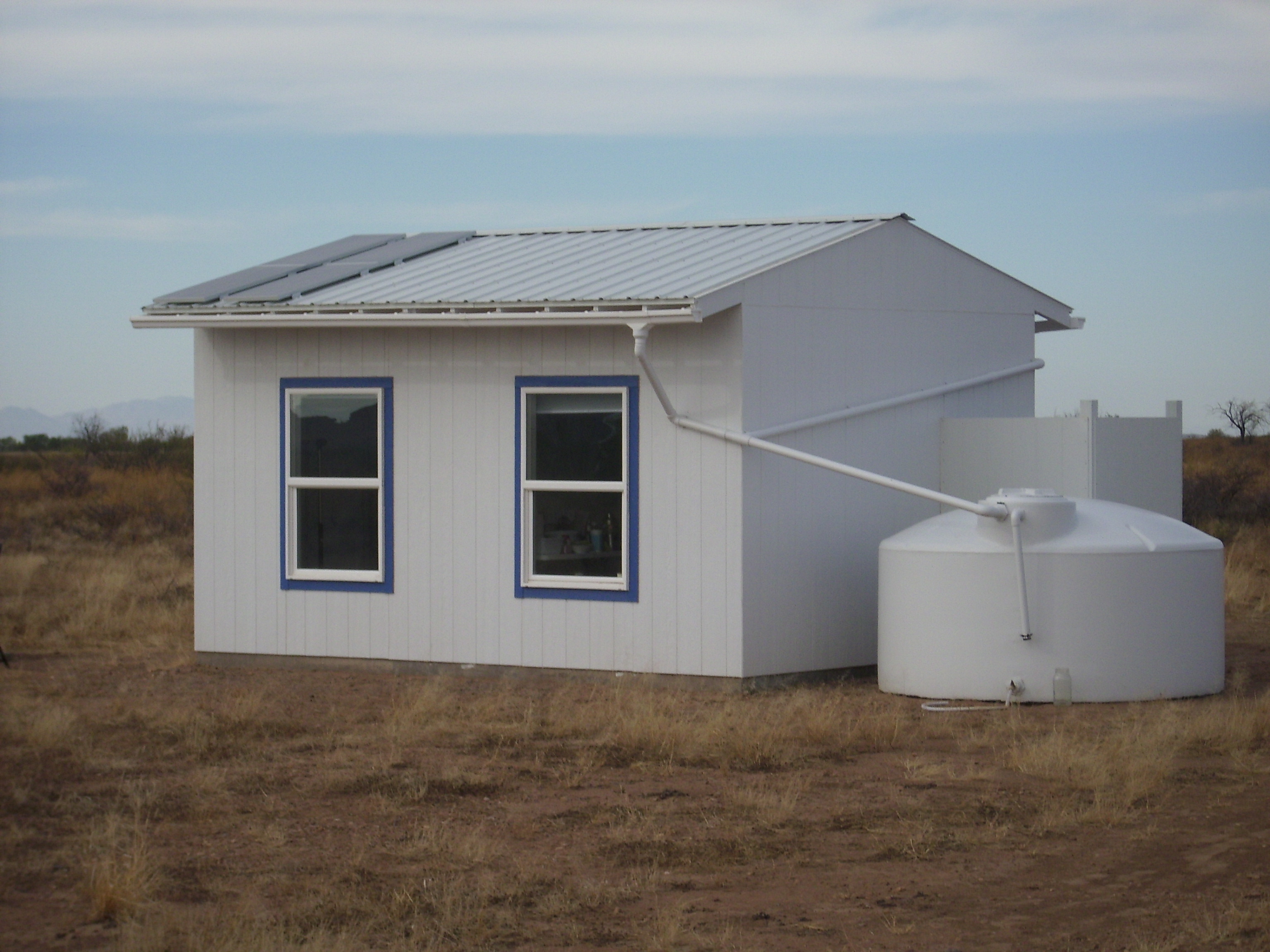 Small white tiny house with solar panels in a dry landscape.