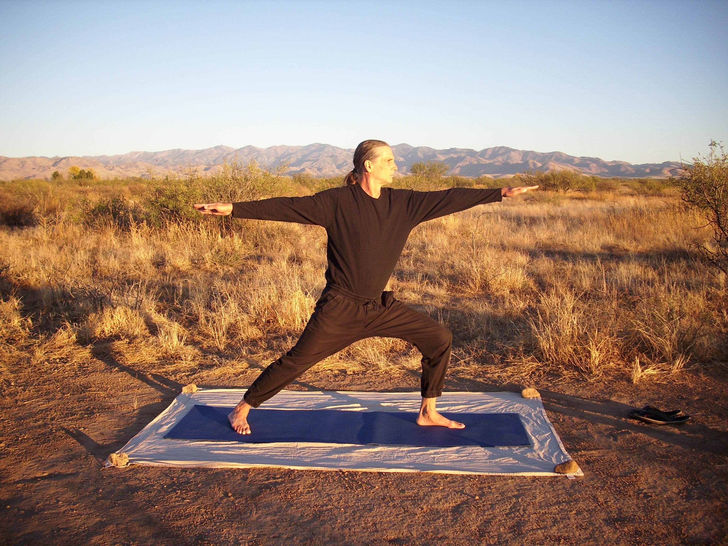 Woman practicing yoga outdoors on a mat in a desert landscape.