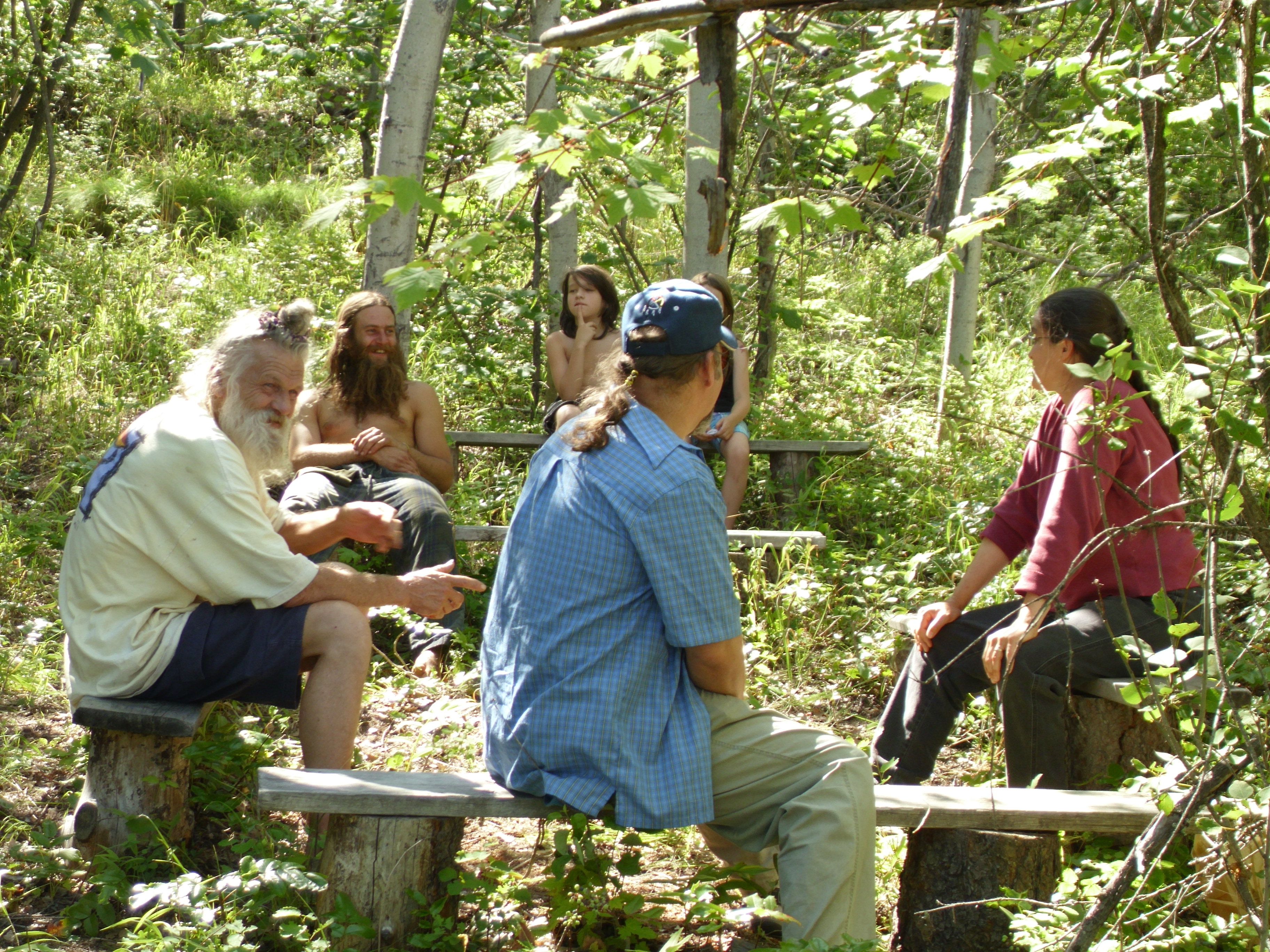 Group of people sitting in a forest clearing during a community event.