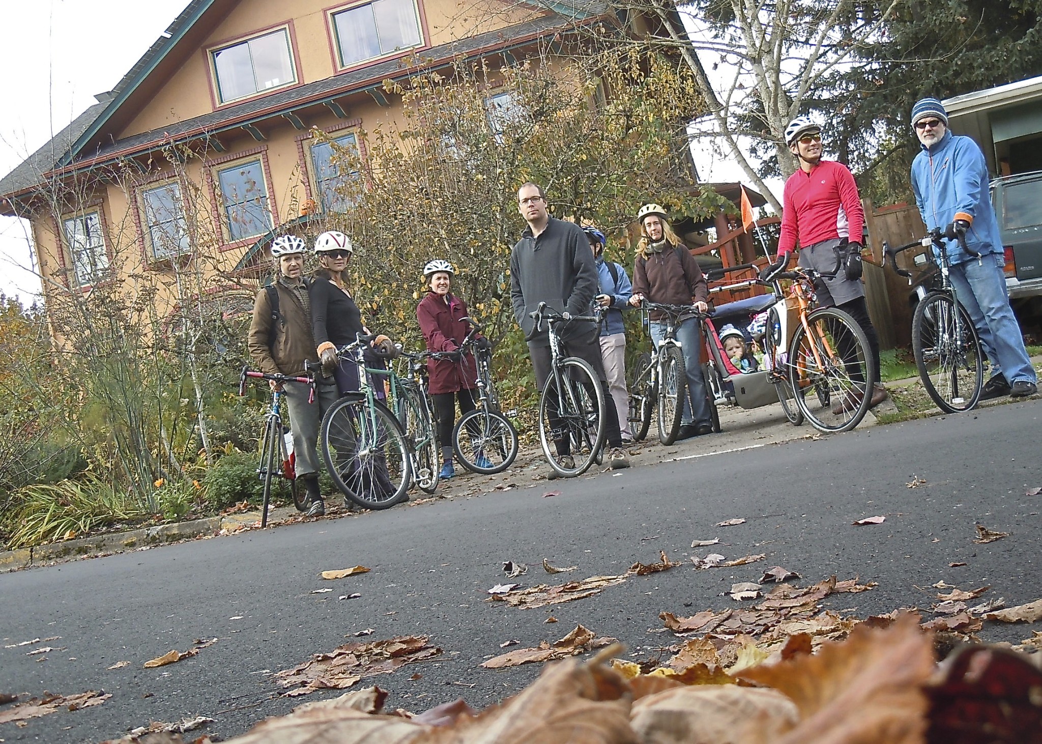 Group of people with bicycles outdoors in front of a house during fall.