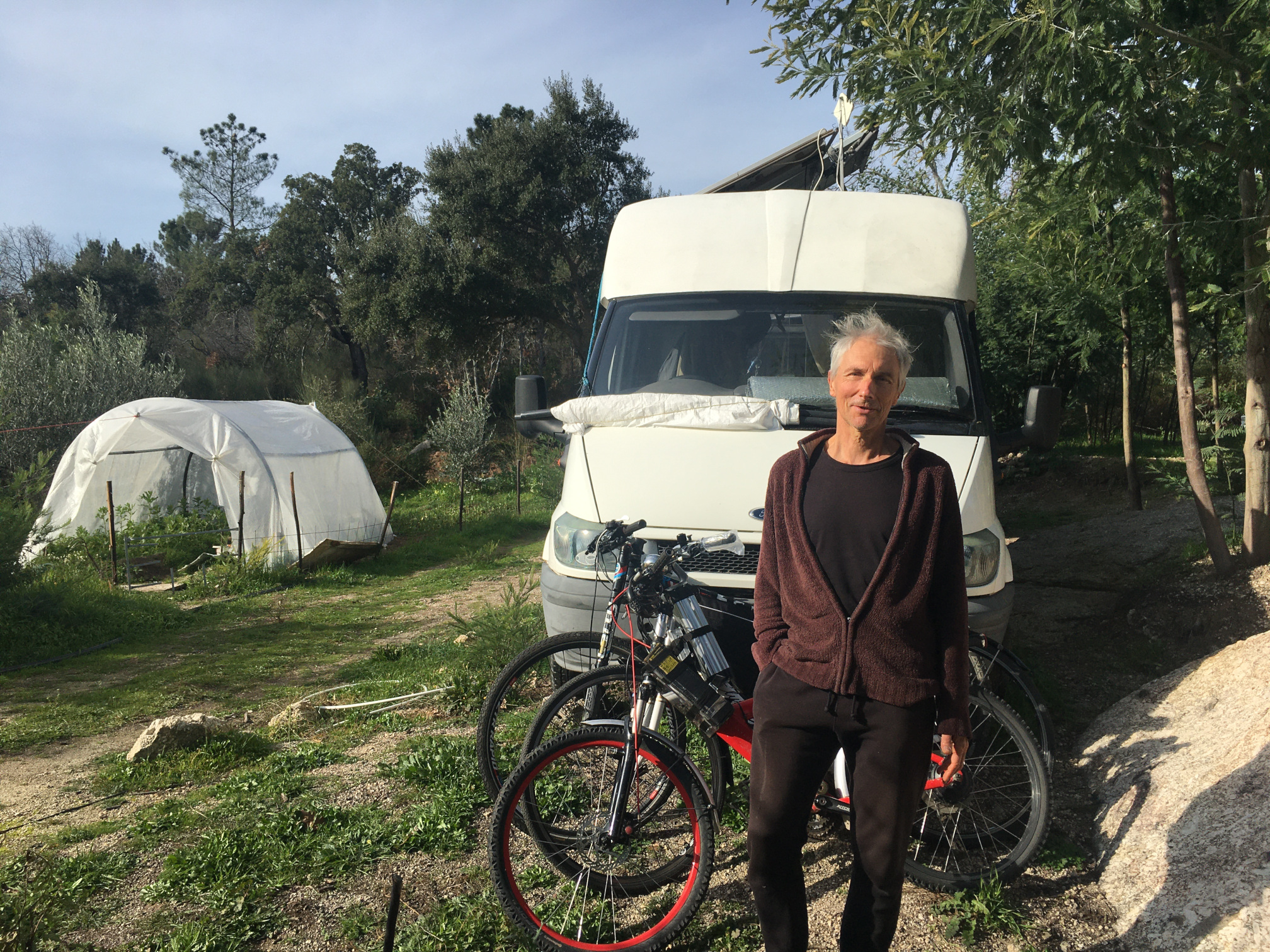 Woman standing with bicycles in front of a camper van in a green outdoor setting.