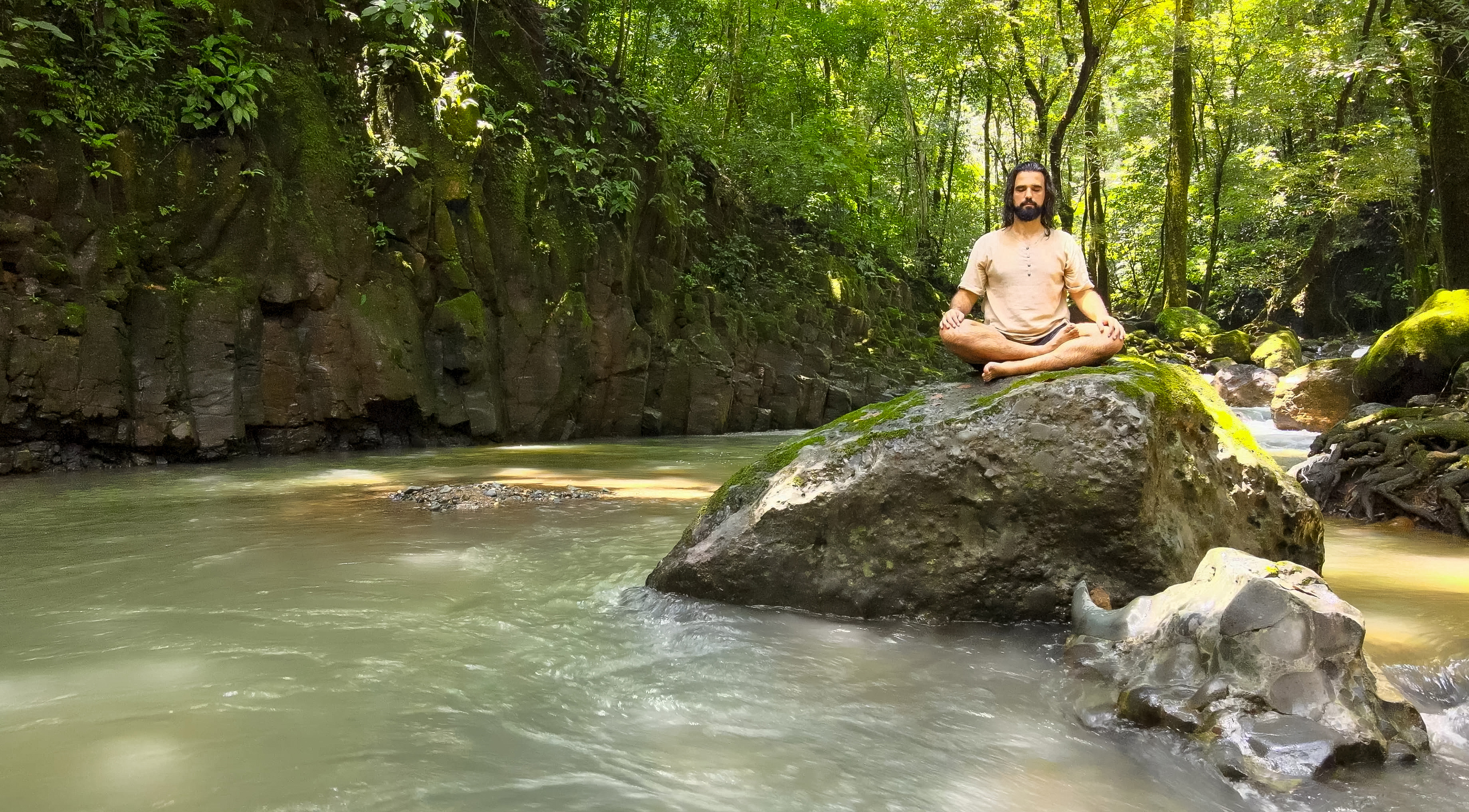 Person meditating on a rock in a lush forest stream in Costa Rica.