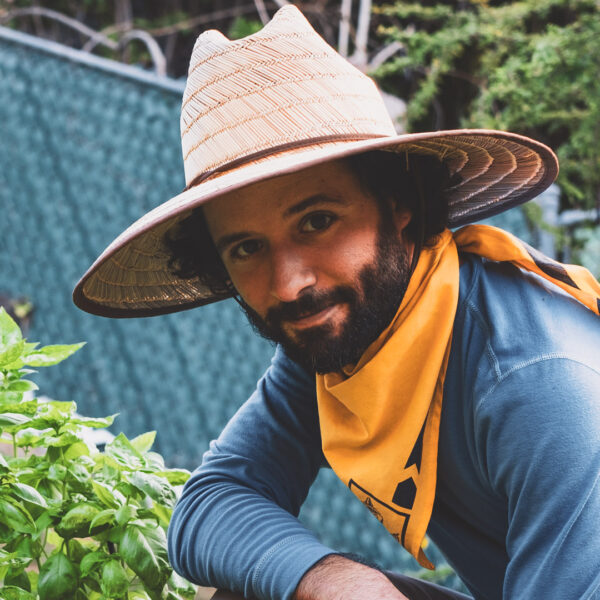 Person gardening in community farm with hat and yellow scarf.
