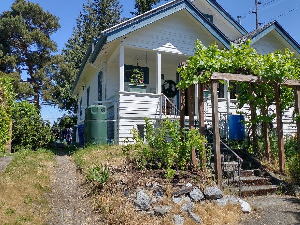 White cottage with front porch and lush garden in a peaceful neighborhood.