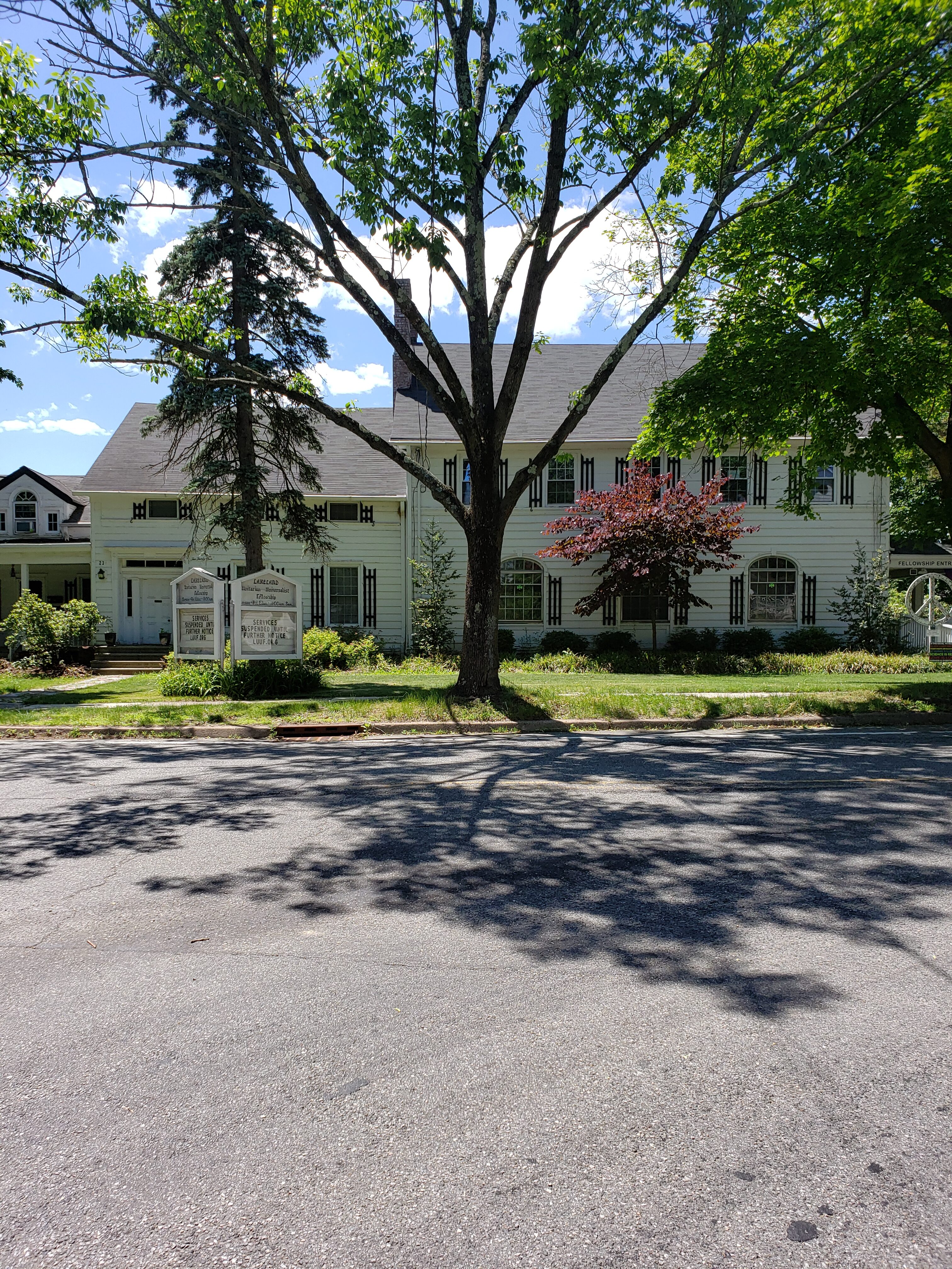 Large tree in front of a white community building with lush greenery.