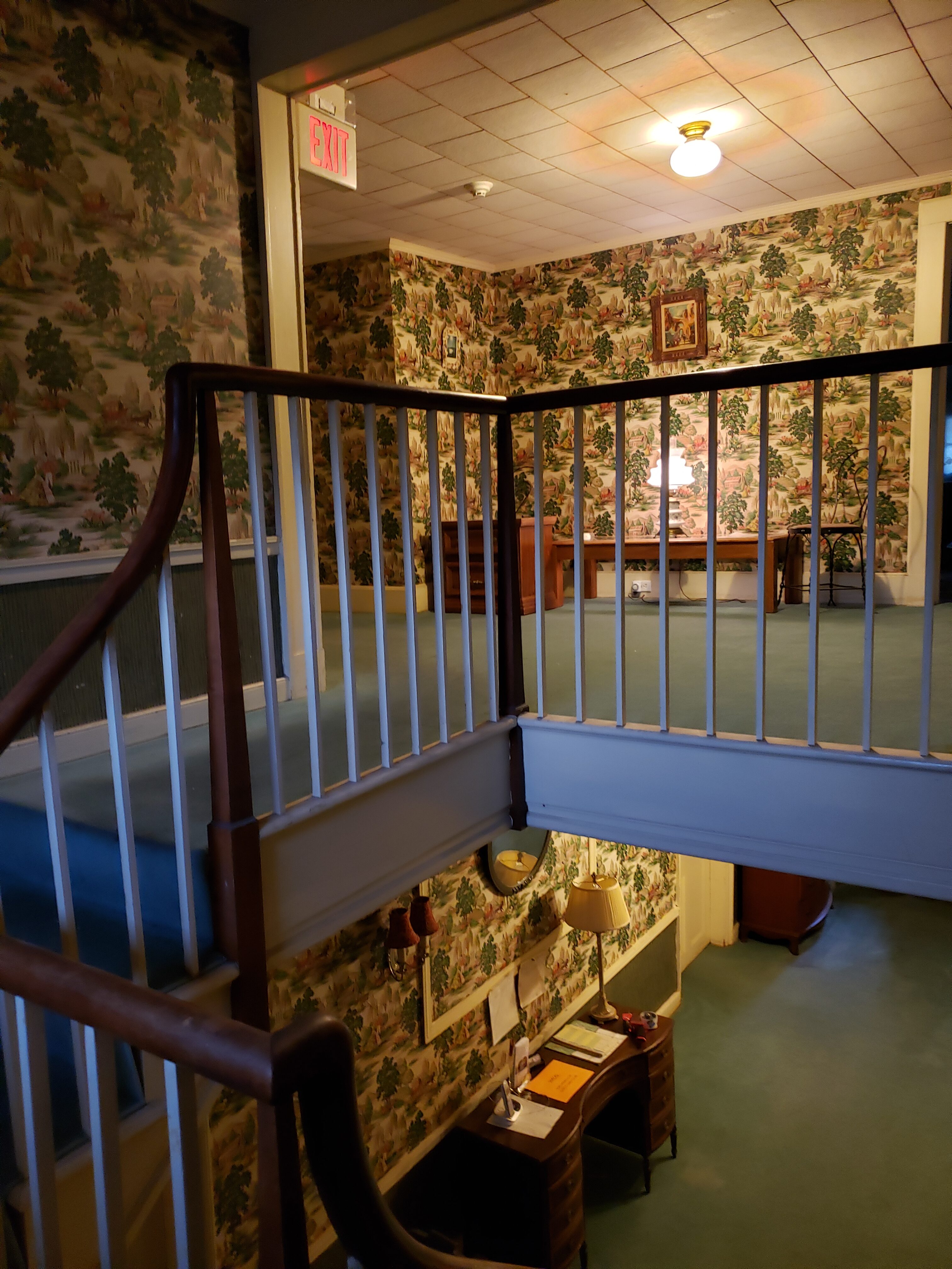 Cozy room with floral wallpaper, wooden furniture, and staircase at Lakeland Unitarian Universalist.