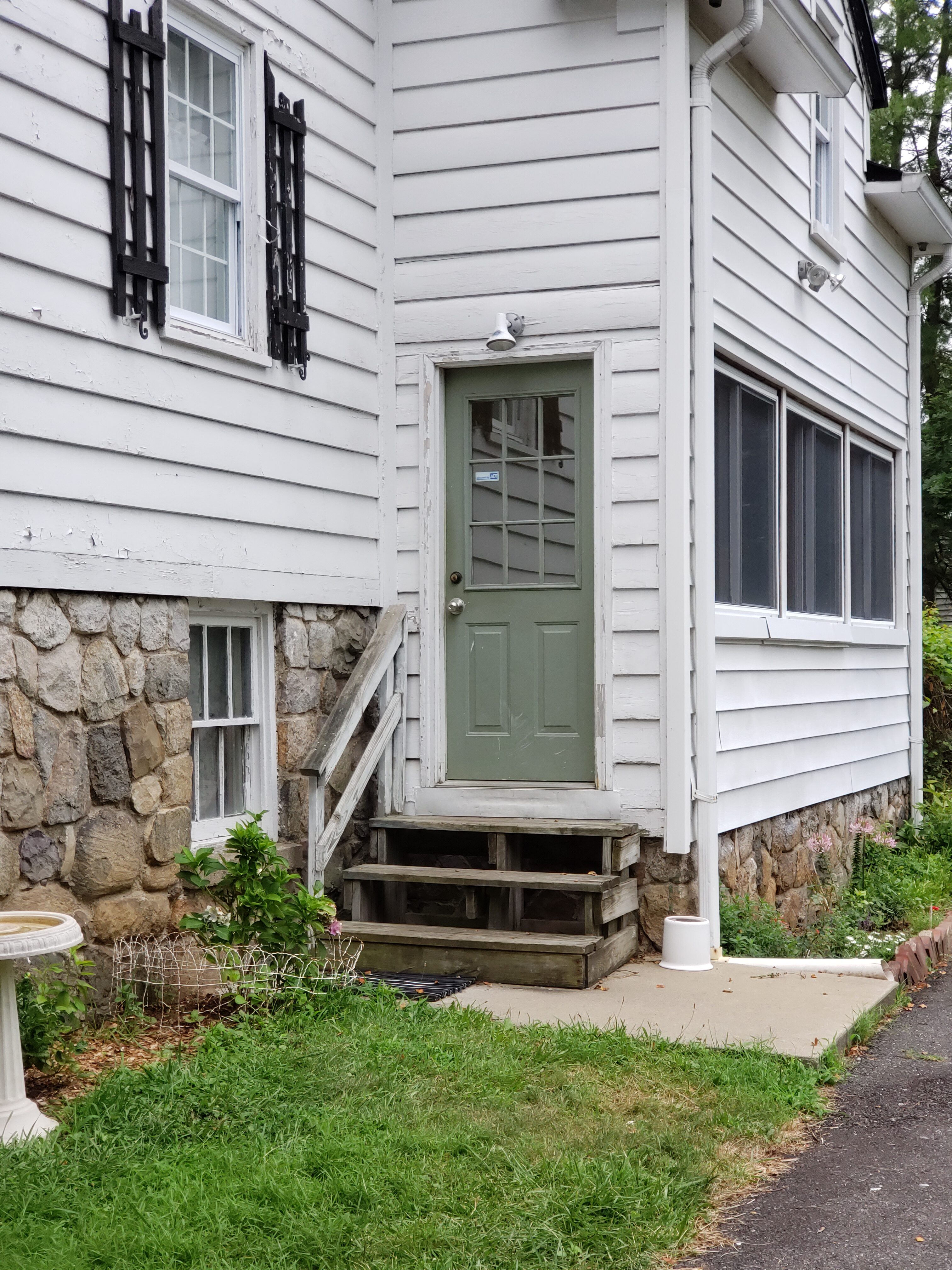Exterior of a white house with a green door and stone foundation.