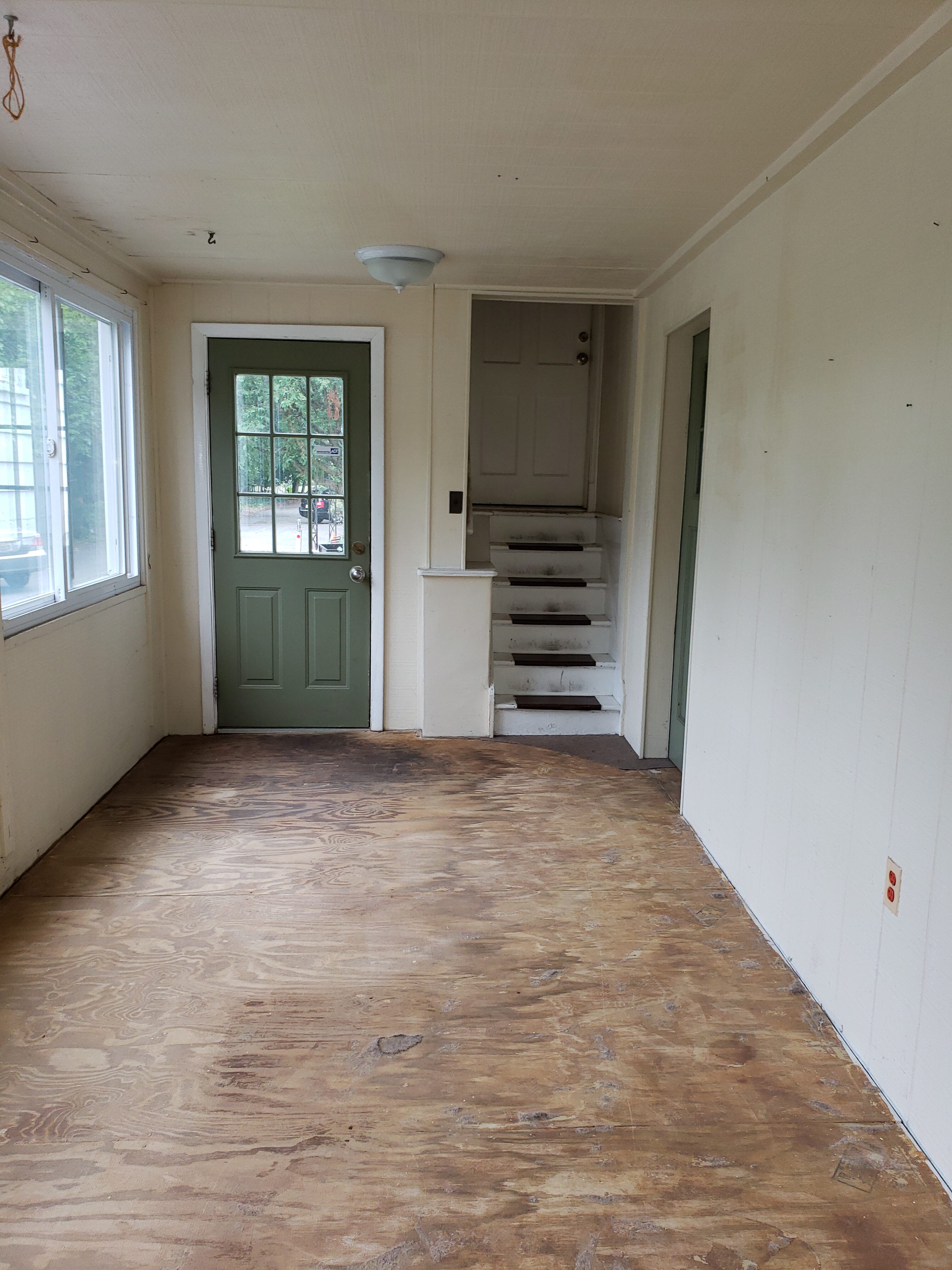 Empty room with wooden floor, green door, and staircase leading upstairs.