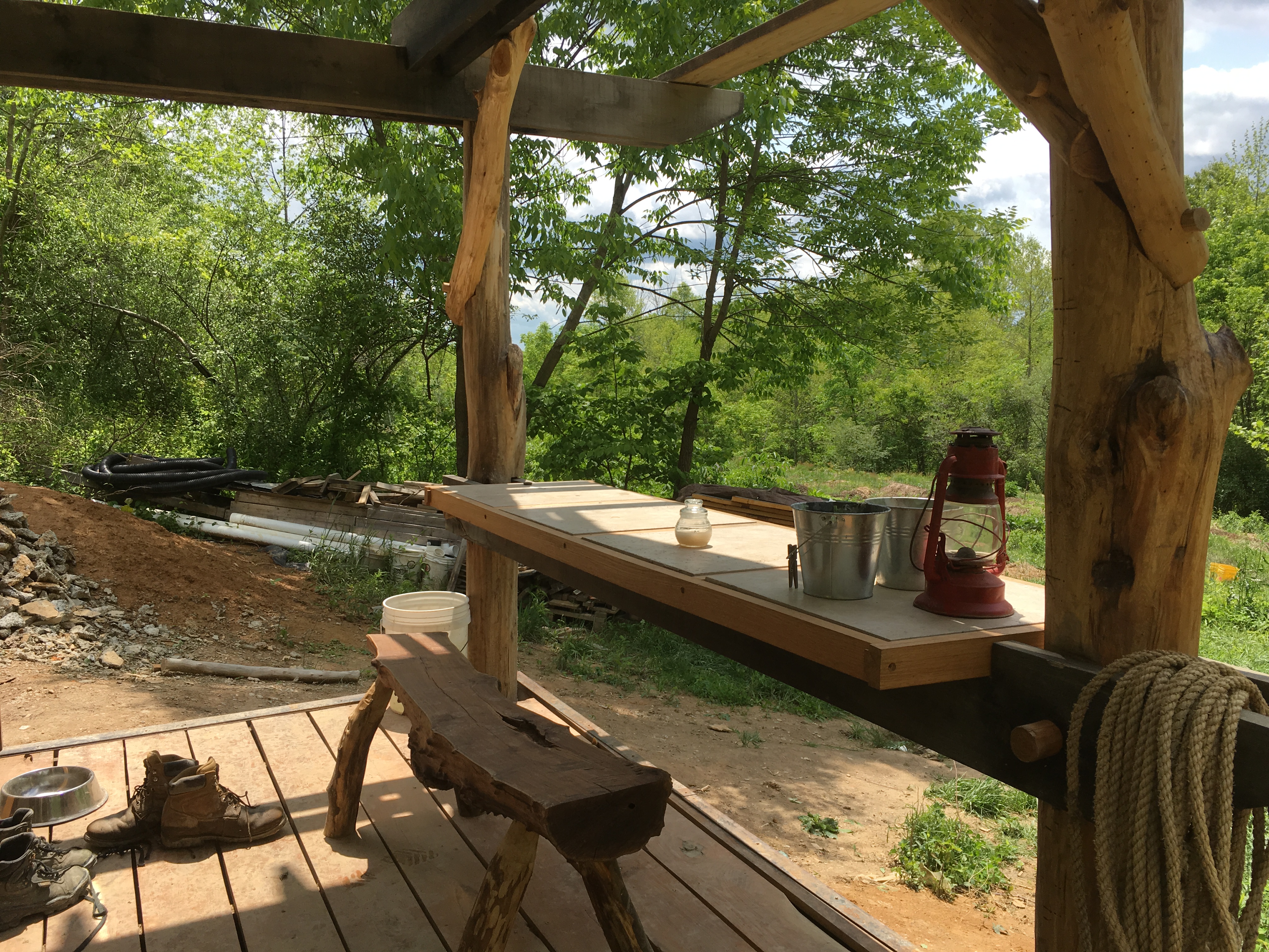 Outdoor rustic kitchen with wooden table, lantern, and cooking utensils in nature.