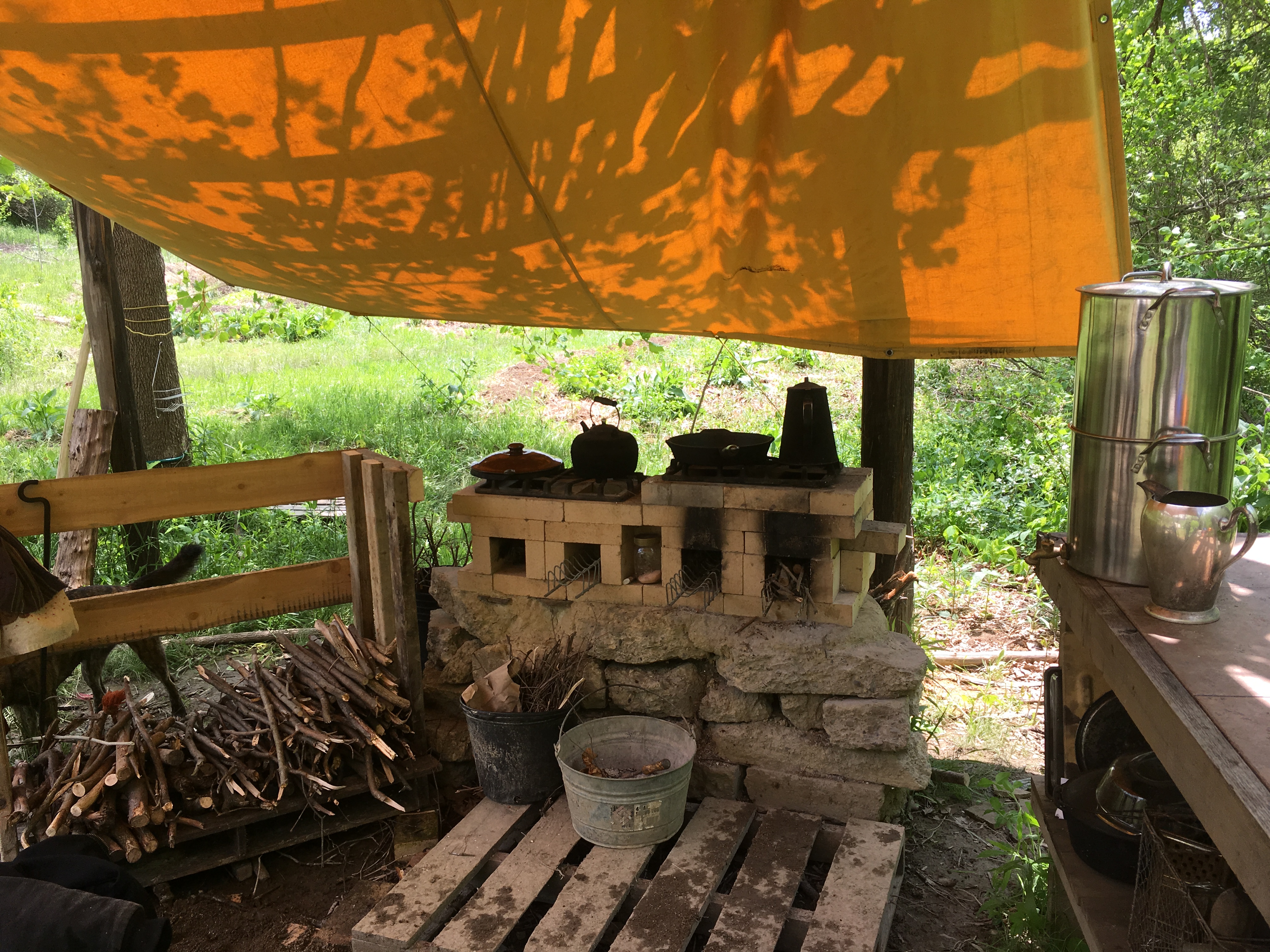 Community outdoor kitchen with makeshift stove and firewood storage.