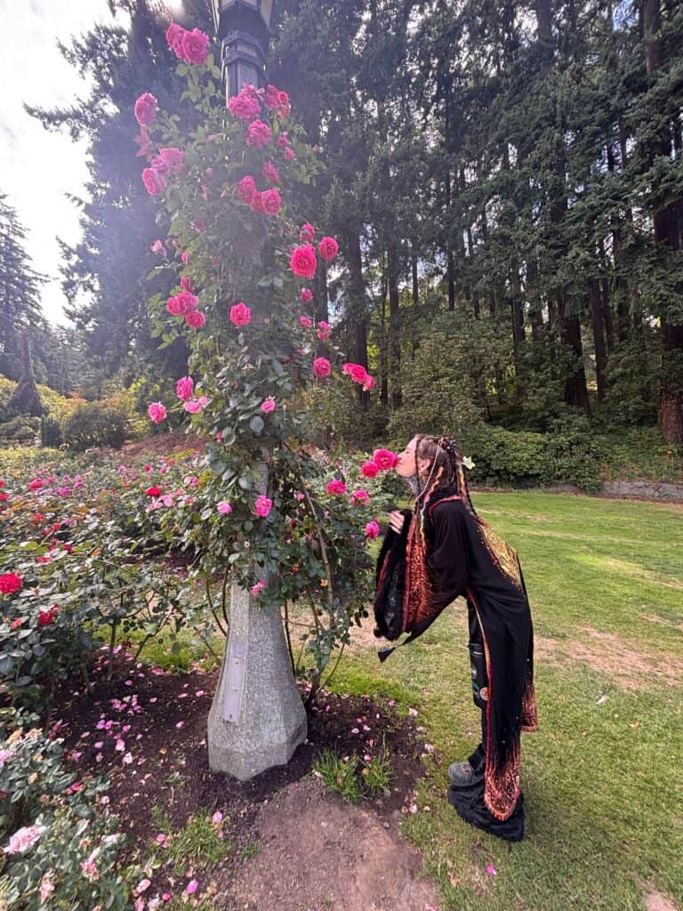 Person smelling pink roses in a lush garden setting.
