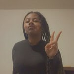 Woman with long dreadlocks making peace sign at community gathering.