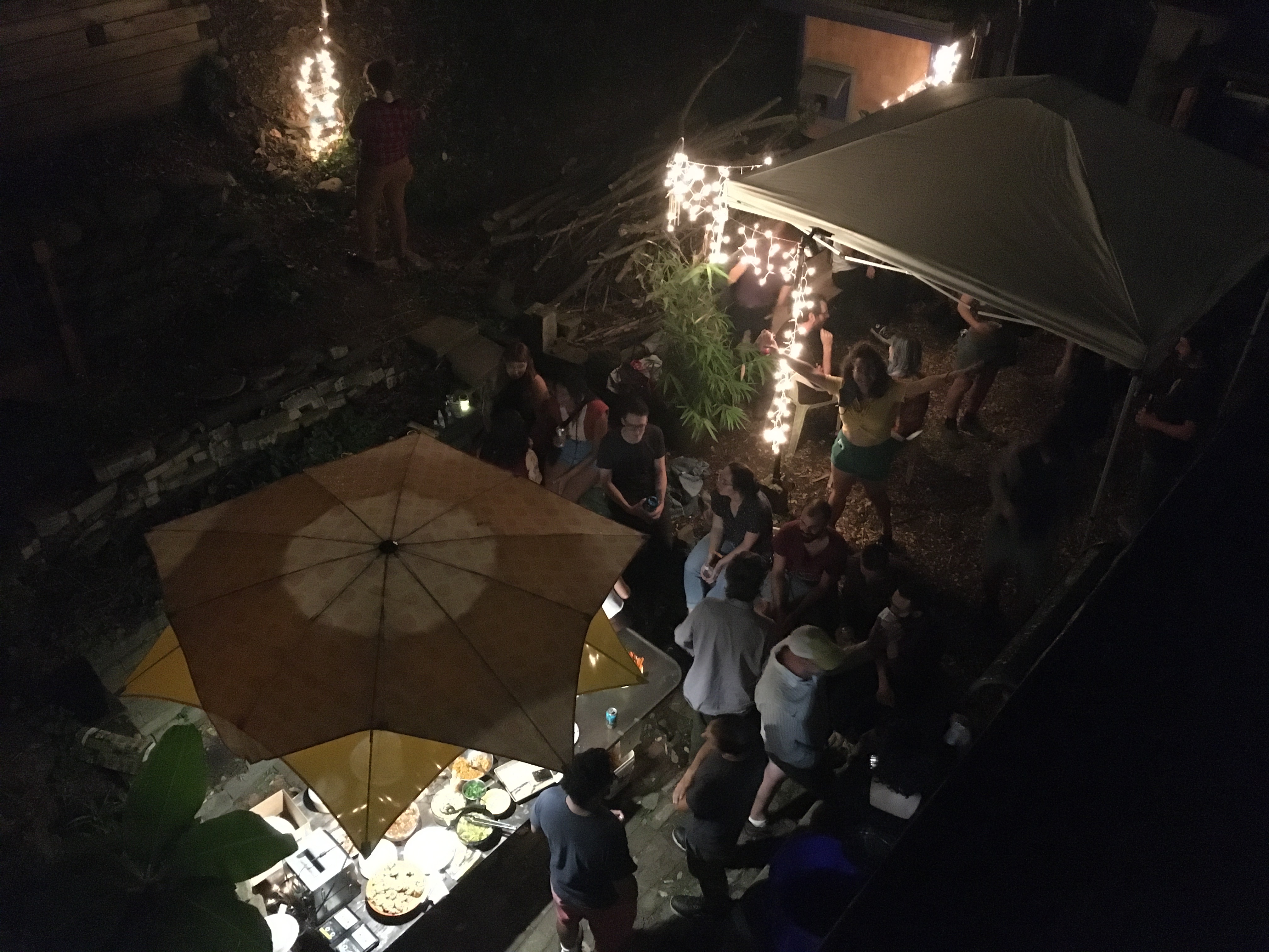 People gathering outdoors with string lights and umbrellas at night.