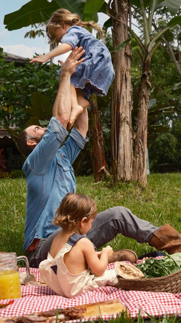 Family playing outdoors, lifting a child in a lush garden setting.