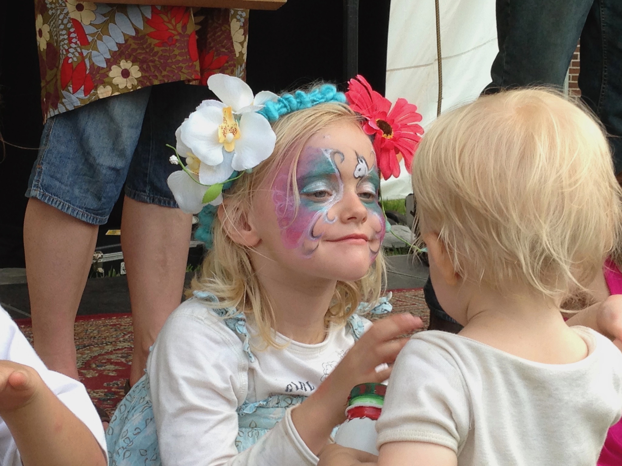 Girl with face paint and floral headband talking to a blonde boy.