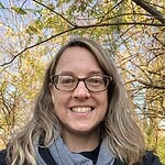 Smiling woman with glasses outdoors in fall foliage.