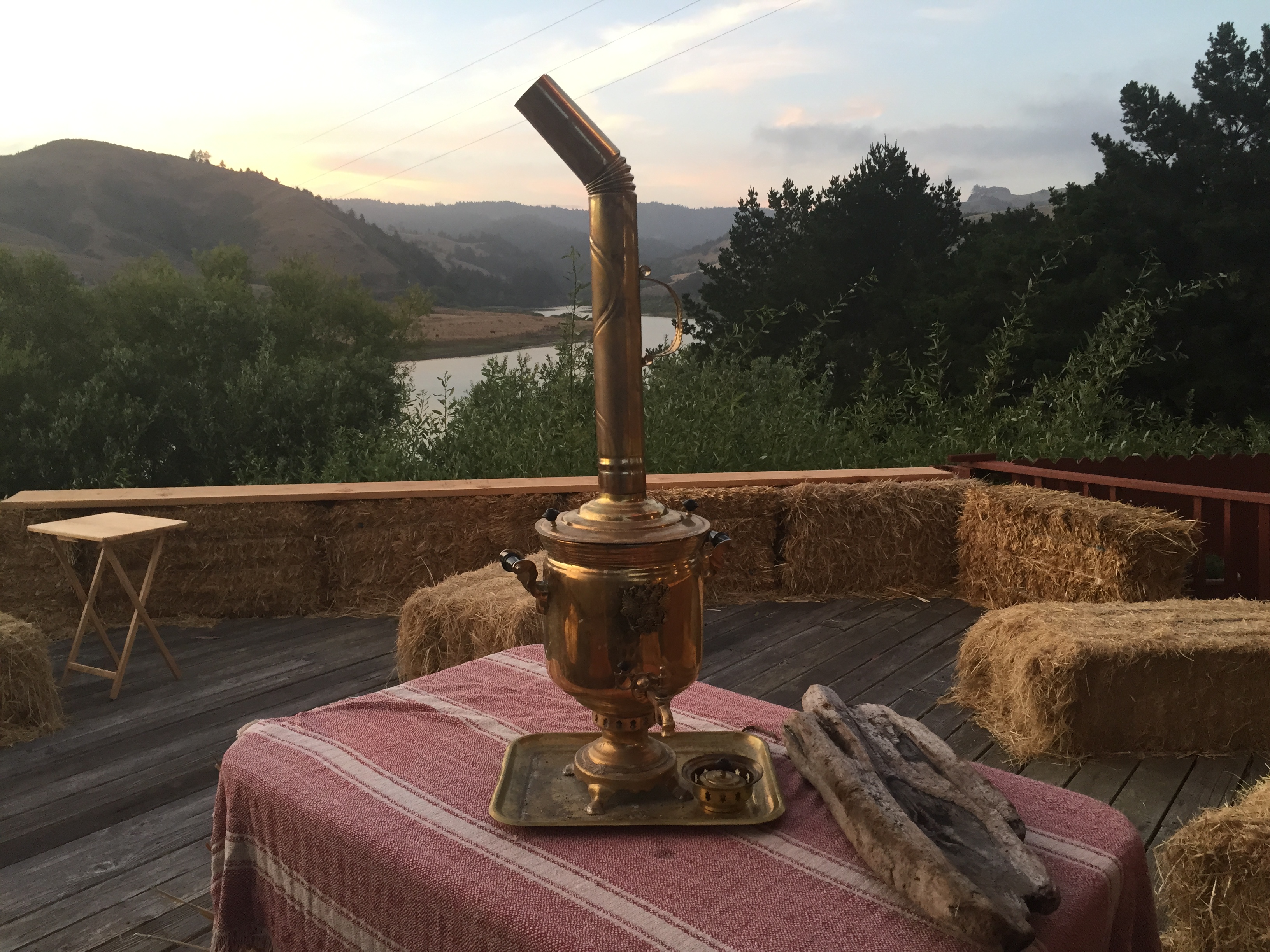 Traditional Russian samovar on outdoor deck with hay bales and scenic landscape.