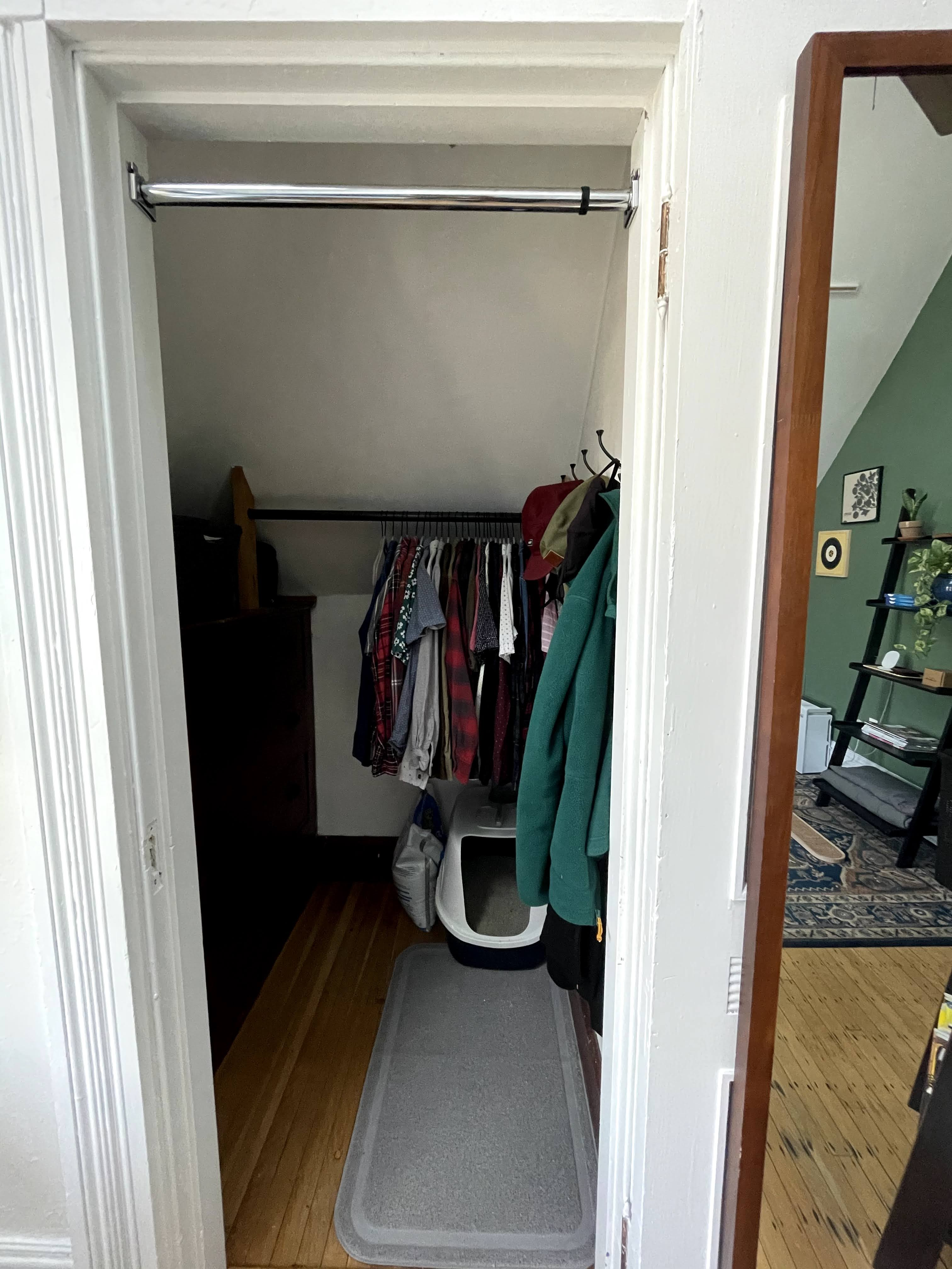 Small closet with hanging clothes and a laundry basket inside.