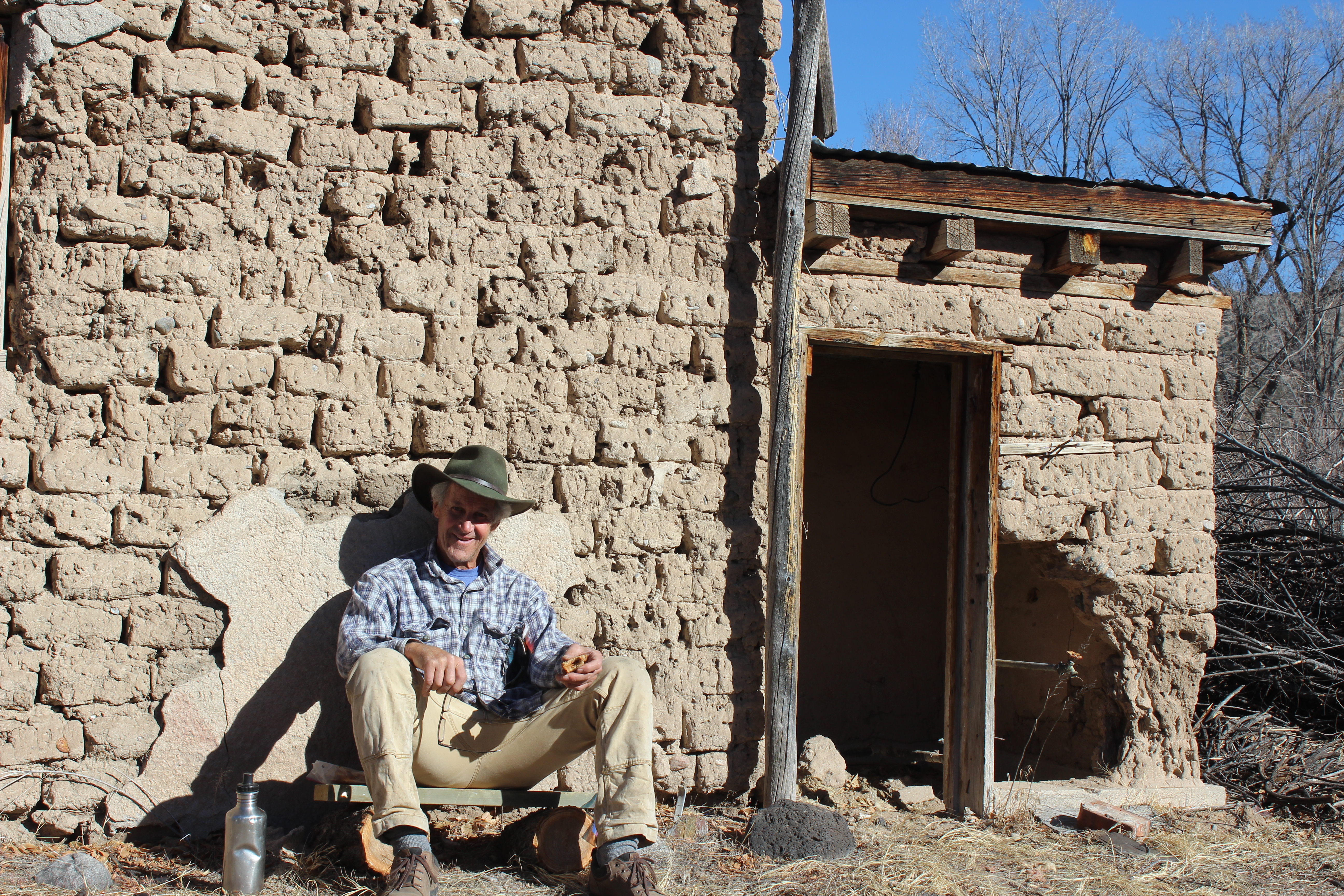 Person sitting outside a rustic adobe building in a community setting.