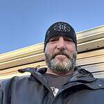 Man wearing a black beanie and outdoor jacket with a John Deere logo.
