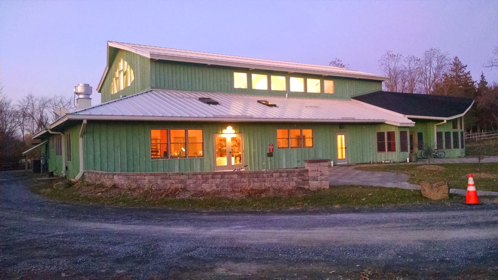 Green community building with large windows and a sloped roof at dusk.