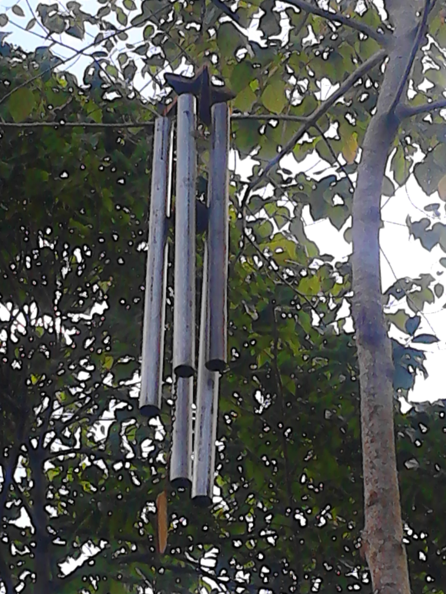 Metal wind chimes hanging from a tree branch in a community setting.
