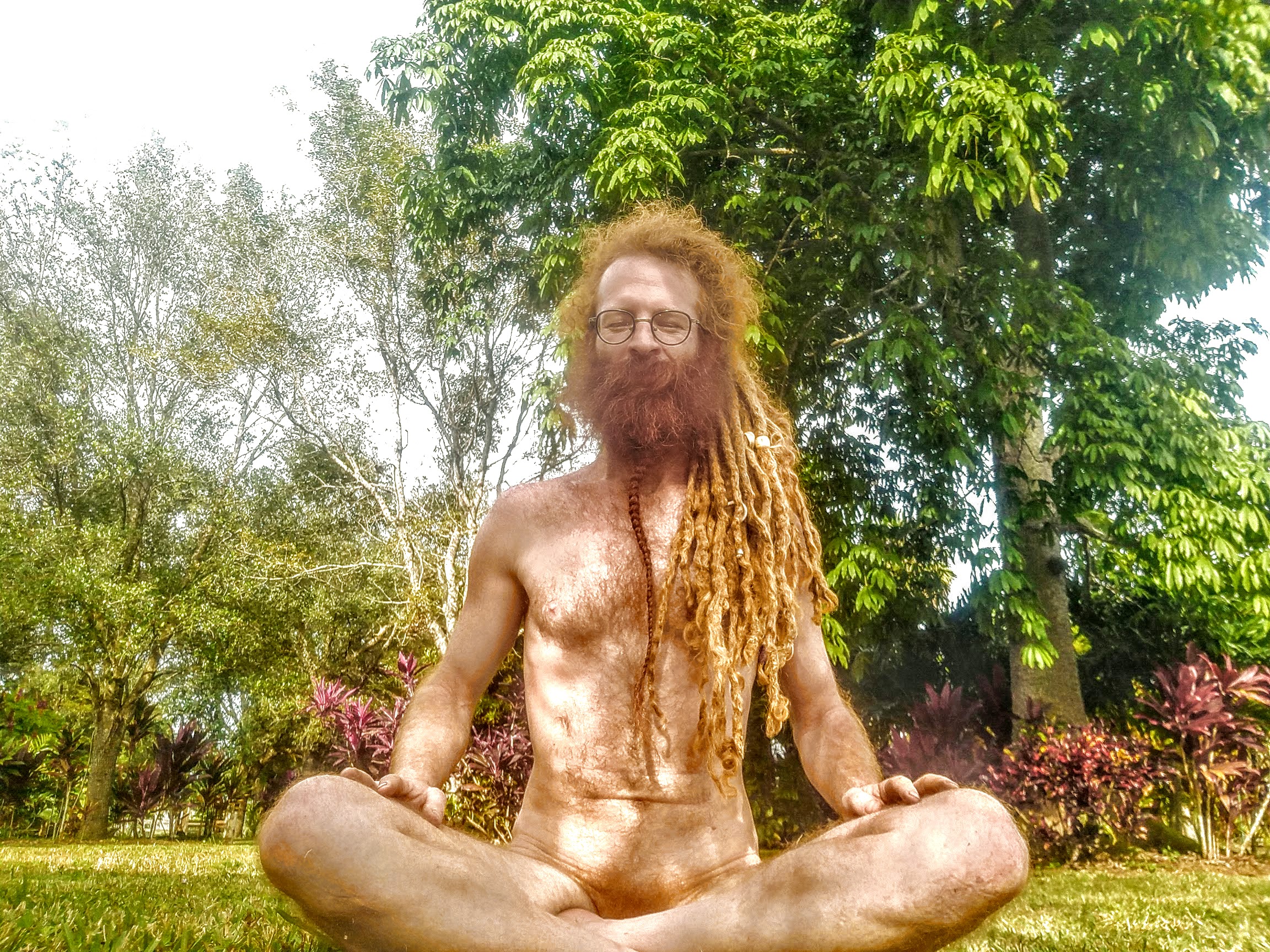 Person with dreadlocks meditating outdoors in a lush garden setting.