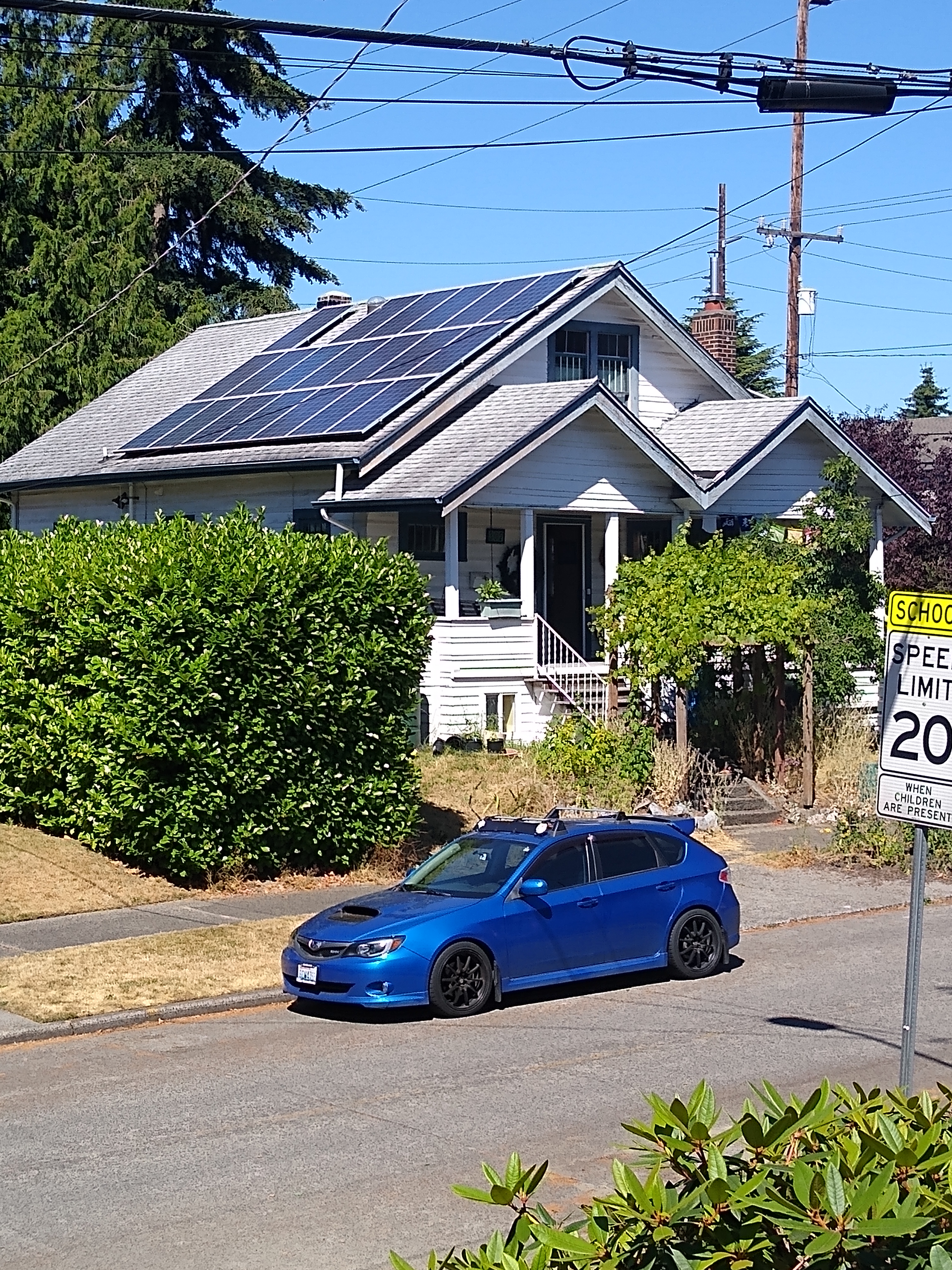House with solar panels on roof and a blue car parked in front.
