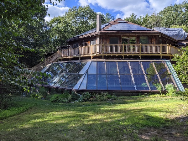Eco-friendly community home with glass and wooden structure in a lush setting.
