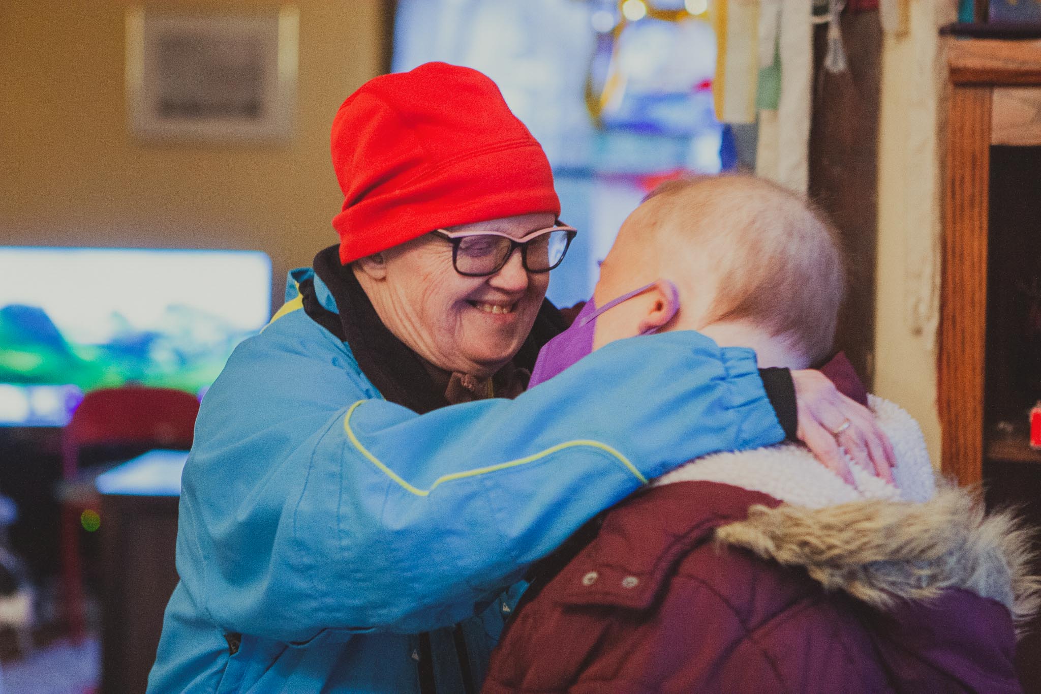 Woman smiling and hugging a child in a warm indoor setting.