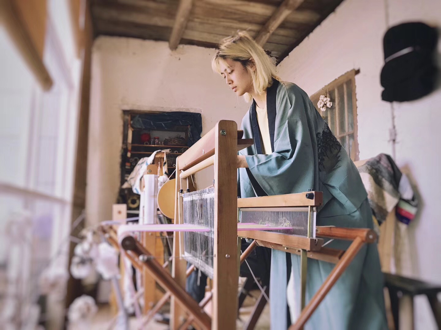 Woman weaving on a loom in a rustic craft room with natural light.