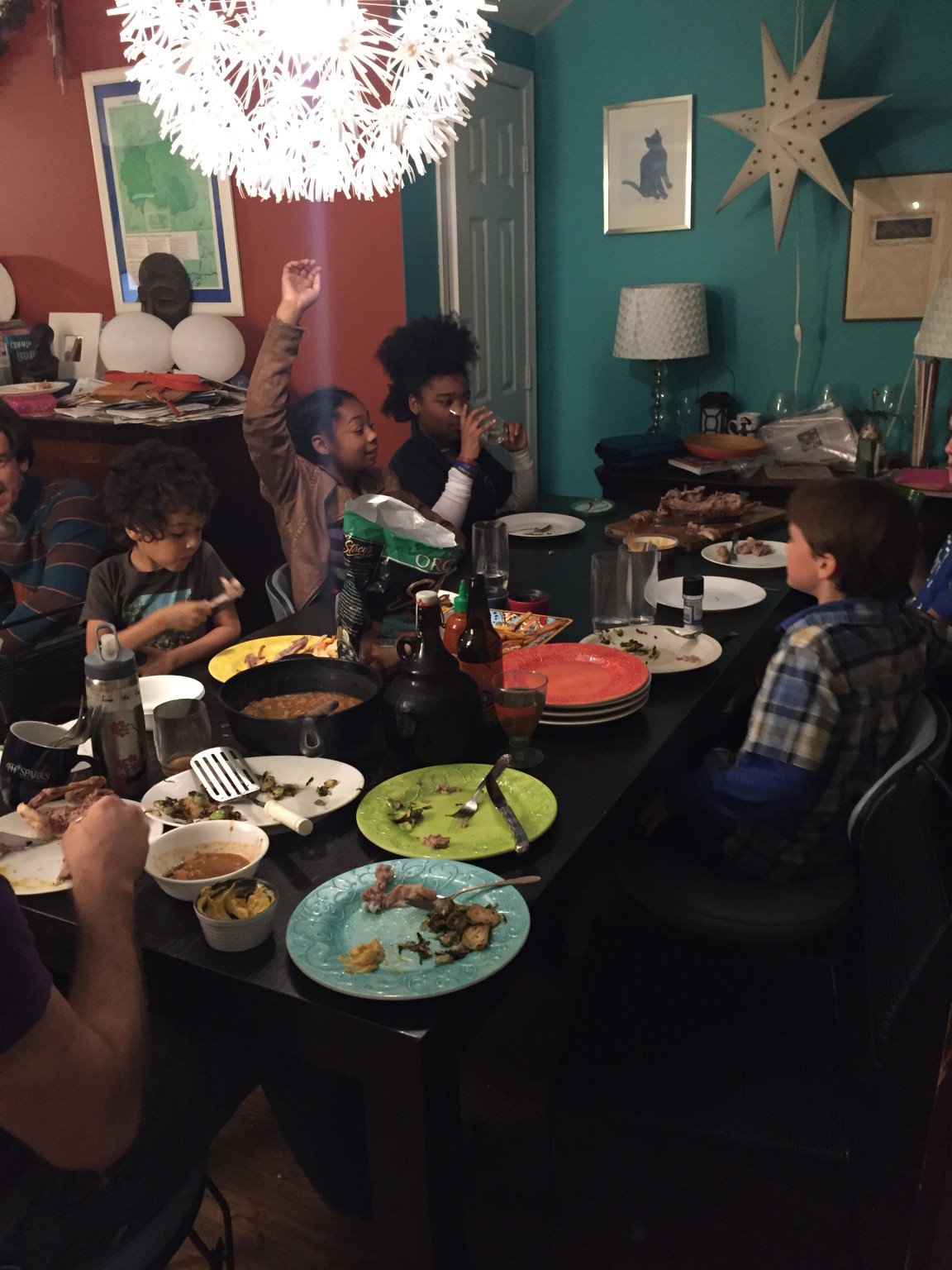 Group of diverse children and adults enjoying a meal together in a cozy home setting.