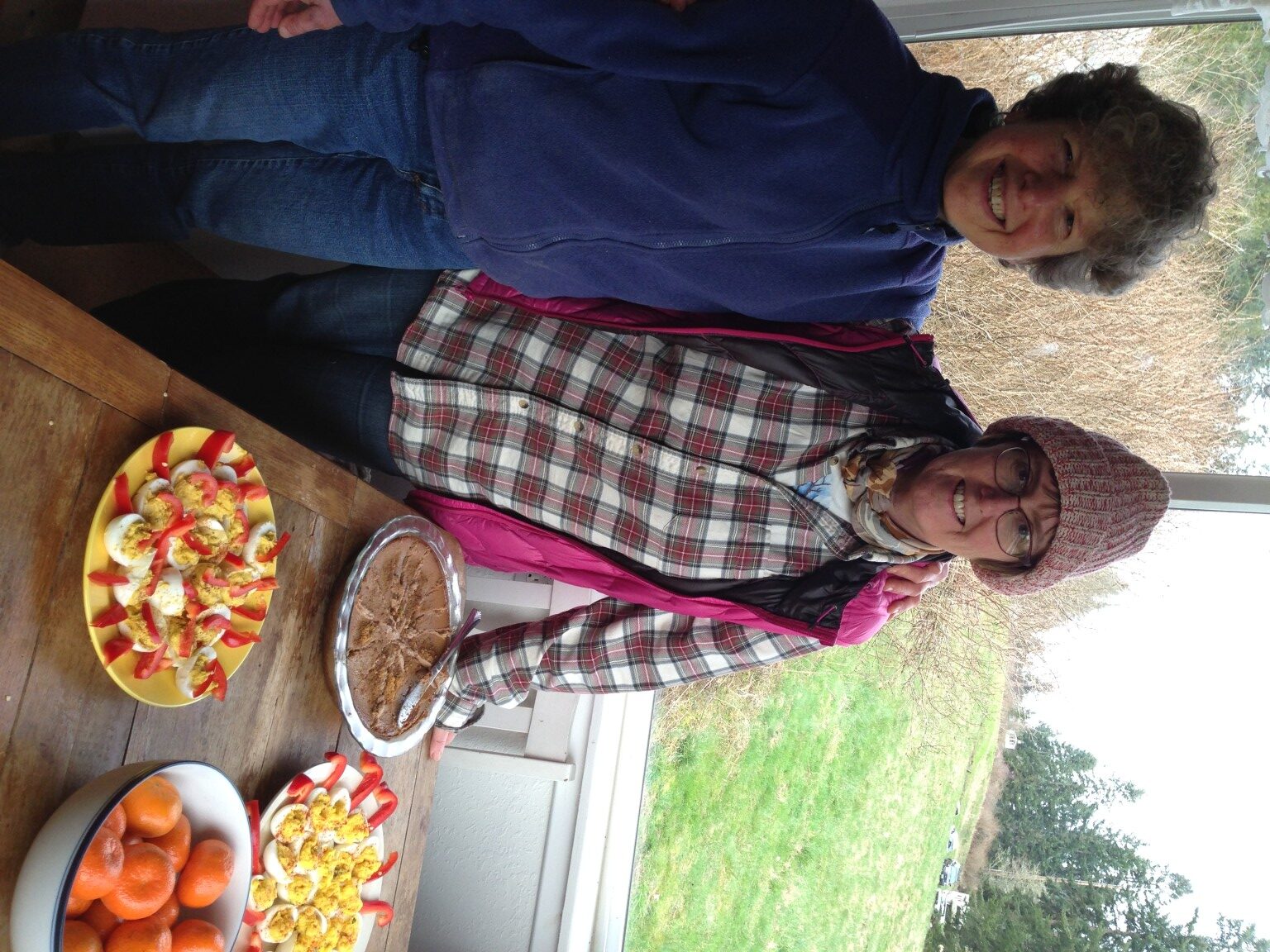 Two women smiling at a community event with snacks on a wooden table.