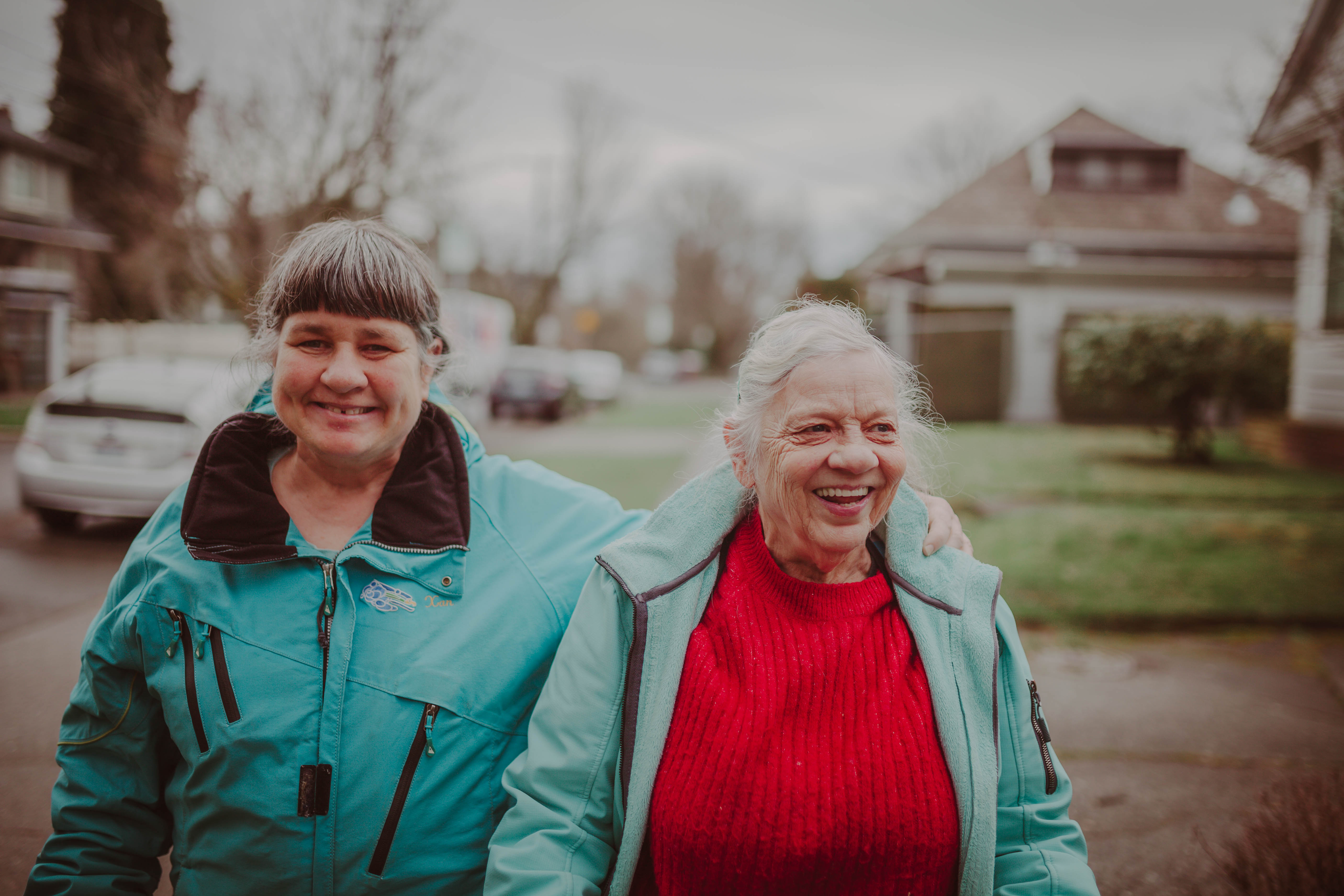 Two women smiling and walking outdoors in a neighborhood setting.
