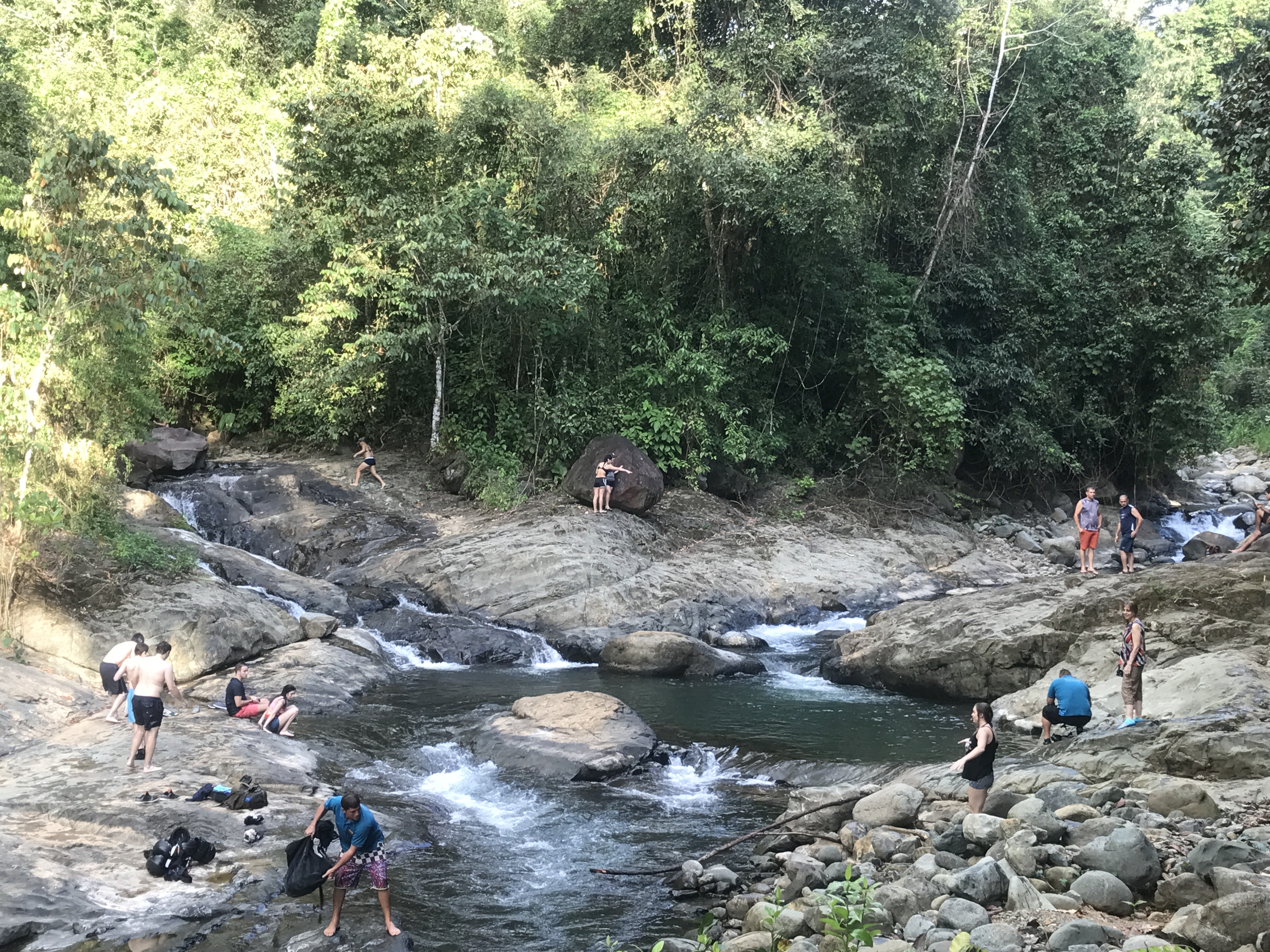 People enjoying a natural river setting with rocks and trees.